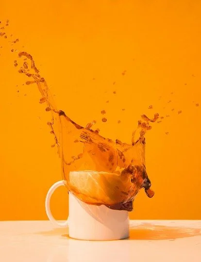 Coffee mug with splash of coffee and liquid splashing out against an orange background.