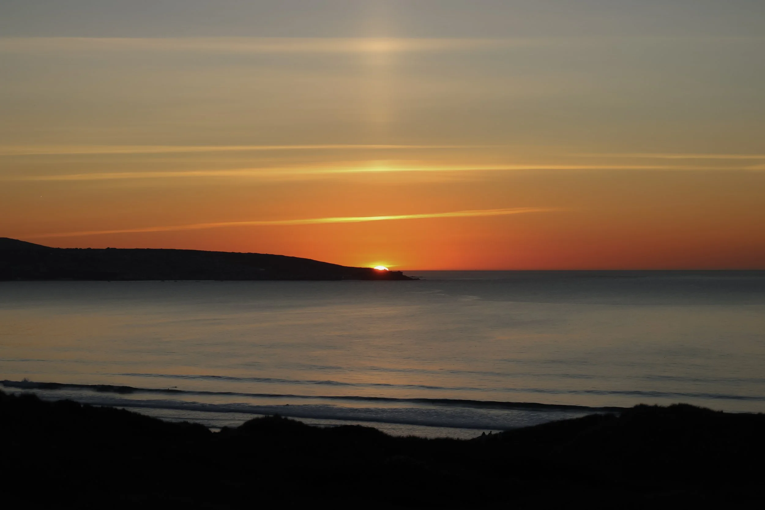 Sunset over ocean with clouds and silhouette of land in the distance