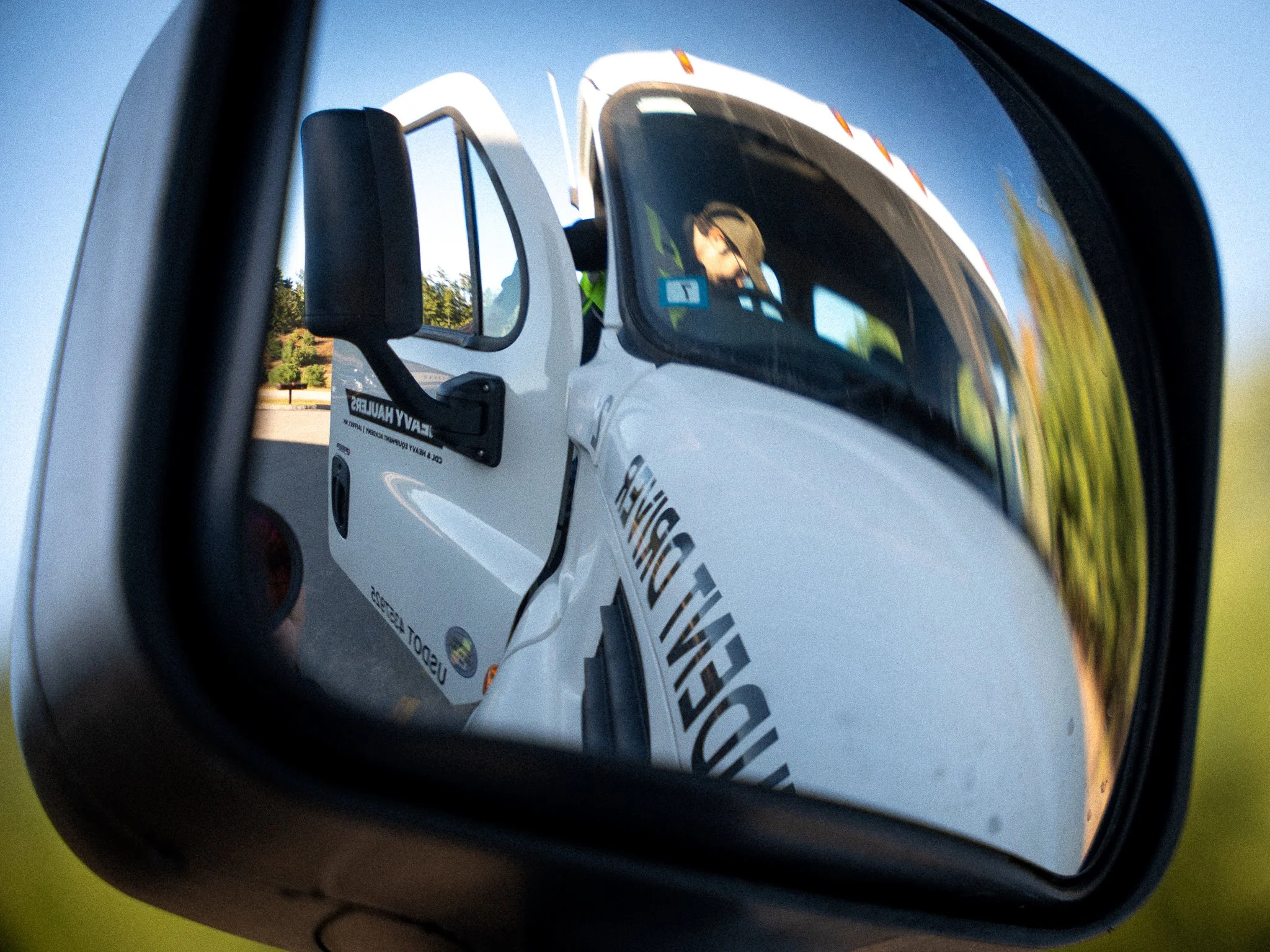 Reflection of a rescue vehicle and a person wearing a yellow vest and a cap seen in a car's side mirror