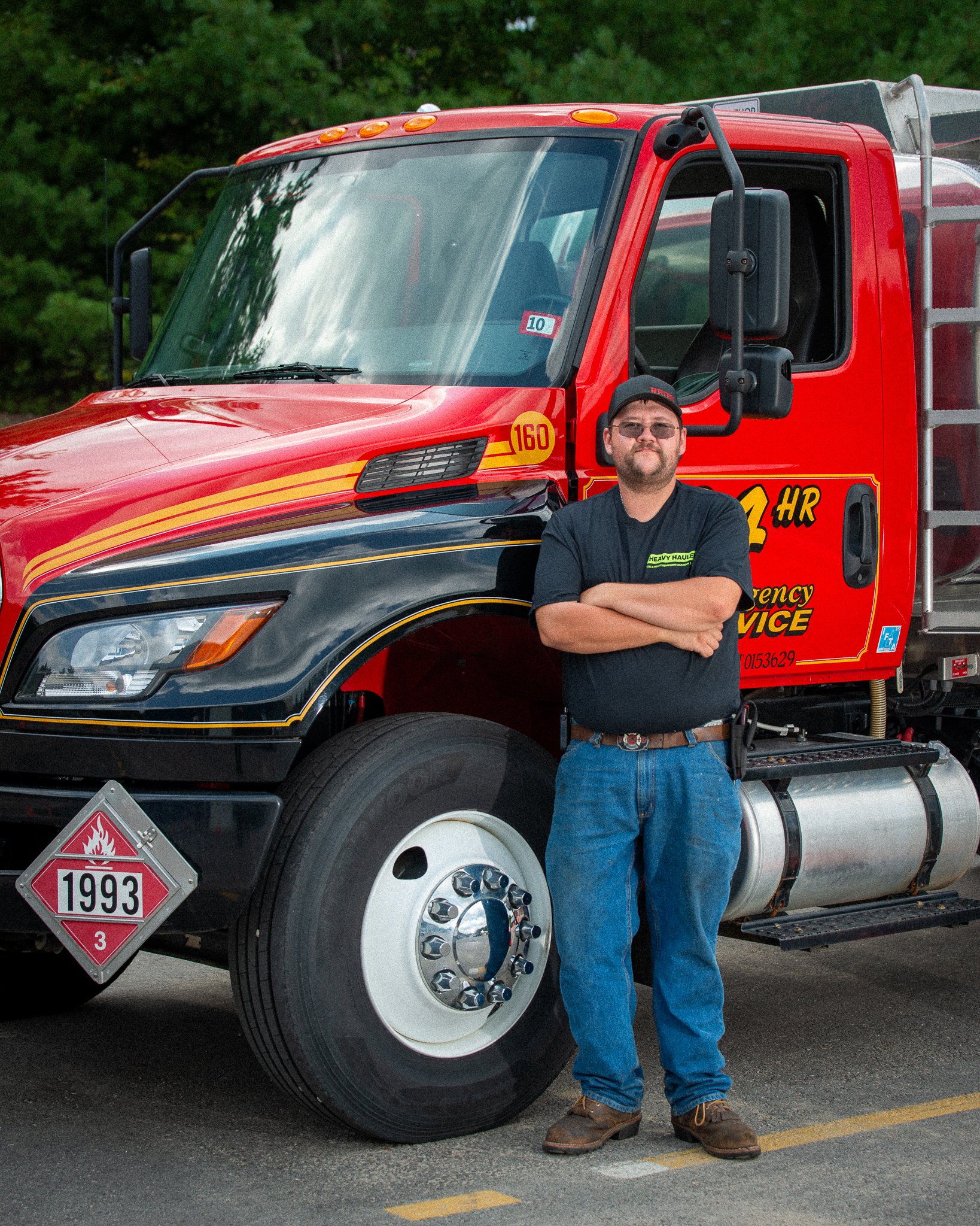 A man standing with arms crossed in front of a red fire truck with emergency service markings and a hazardous materials sign.