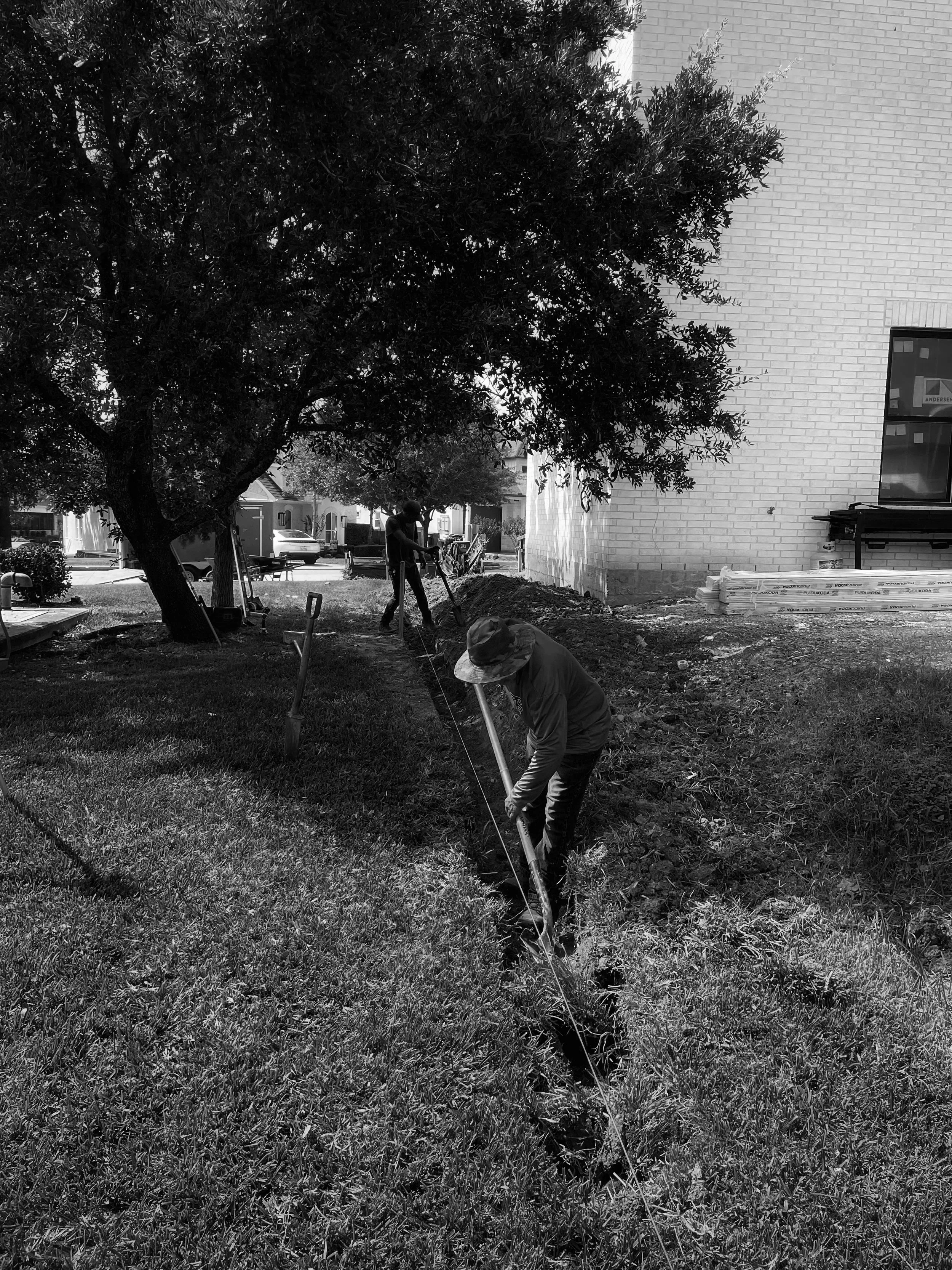 Two workers are digging a trench to build a retaining wall for new construction property.