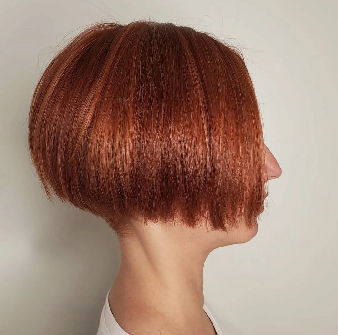 Side view of a woman with a short, sleek, vibrant red bob haircut.
