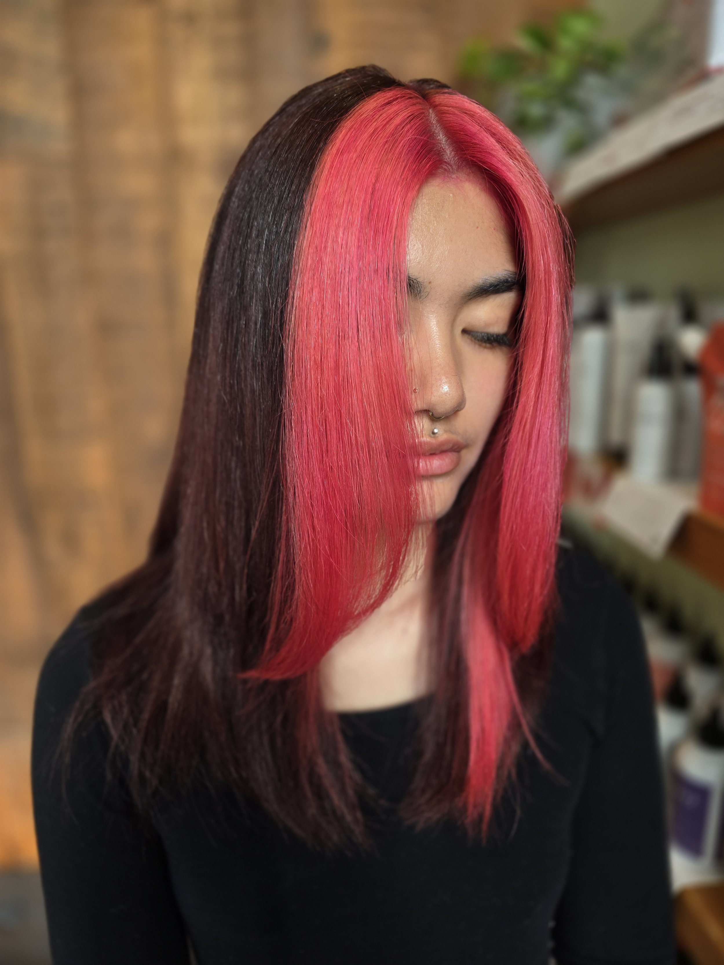 A woman with shoulder-length hair styled in a bold two-tone color, with the front section bright pink and the rest dark brown.