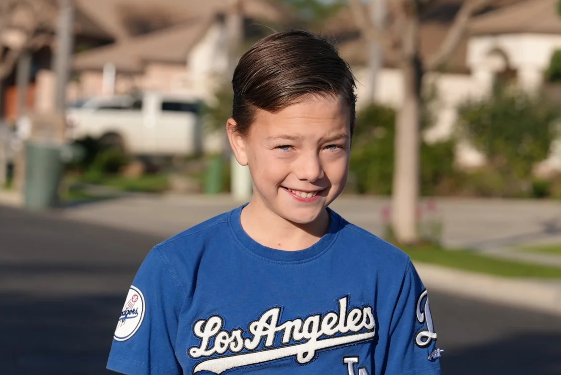 A young boy with dark hair smiling outdoors, wearing a turquoise and red Levi's shirt.