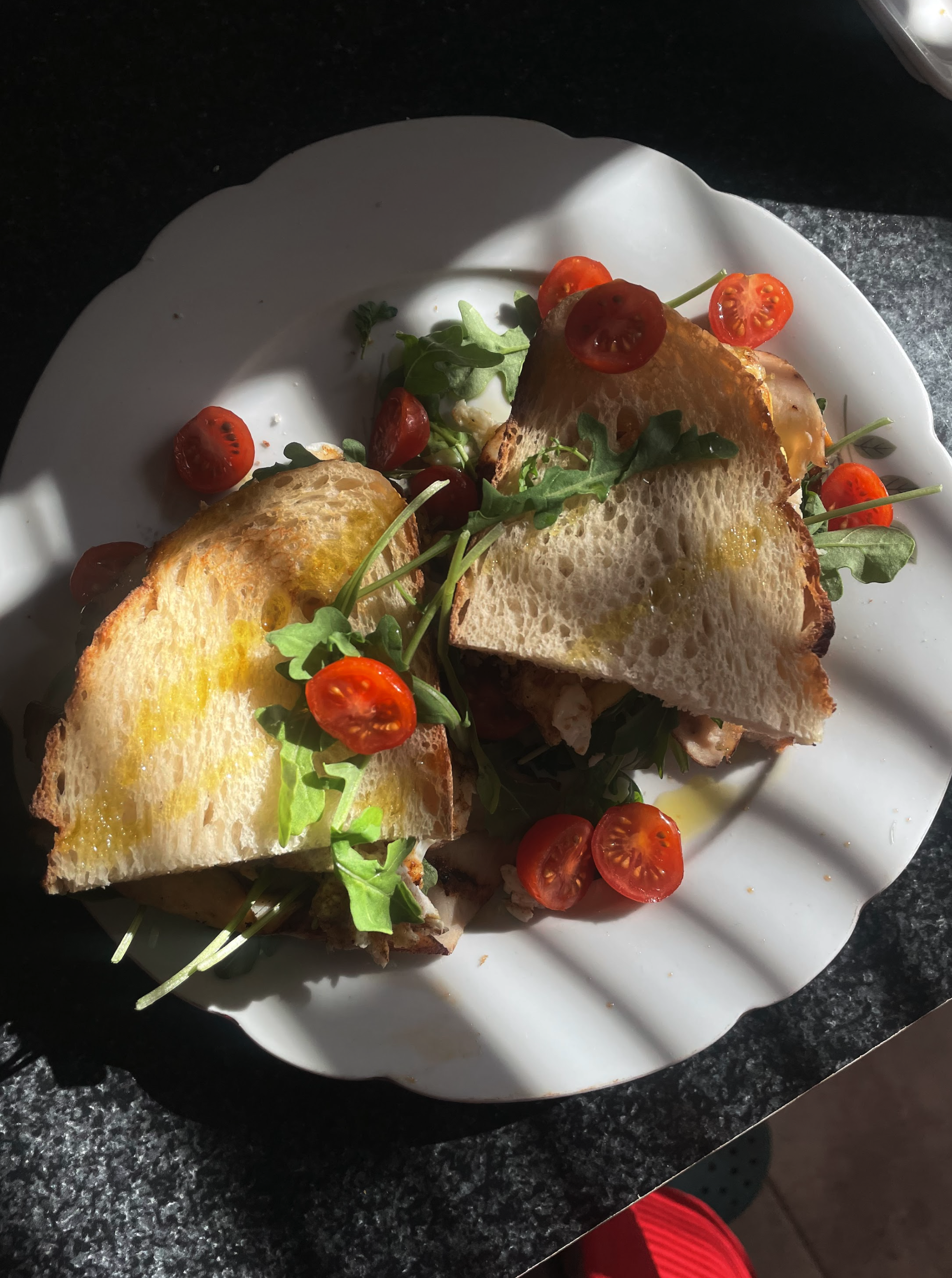 A white plate with a sandwich and cherry tomatoes on a dark countertop.