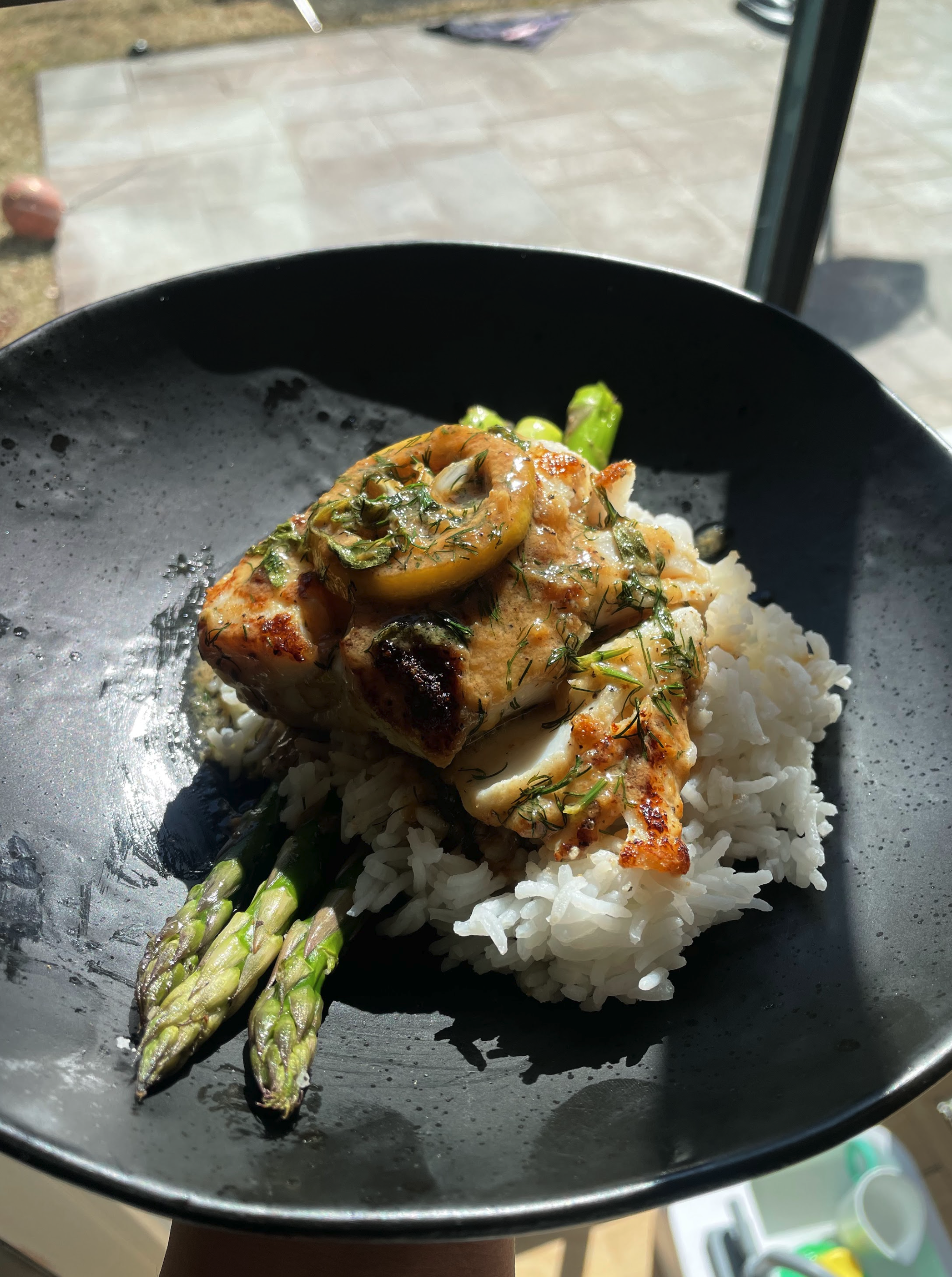 A black bowl of cooked white rice topped with grilled chicken, sliced mushrooms, herbs, and green chopped vegetables, with cooked asparagus spears placed underneath the chicken.