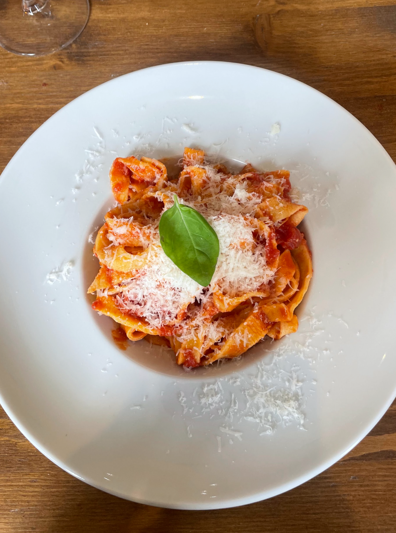 Plate of pasta with tomato sauce, grated cheese, and a basil leaf garnish on a wooden table.
