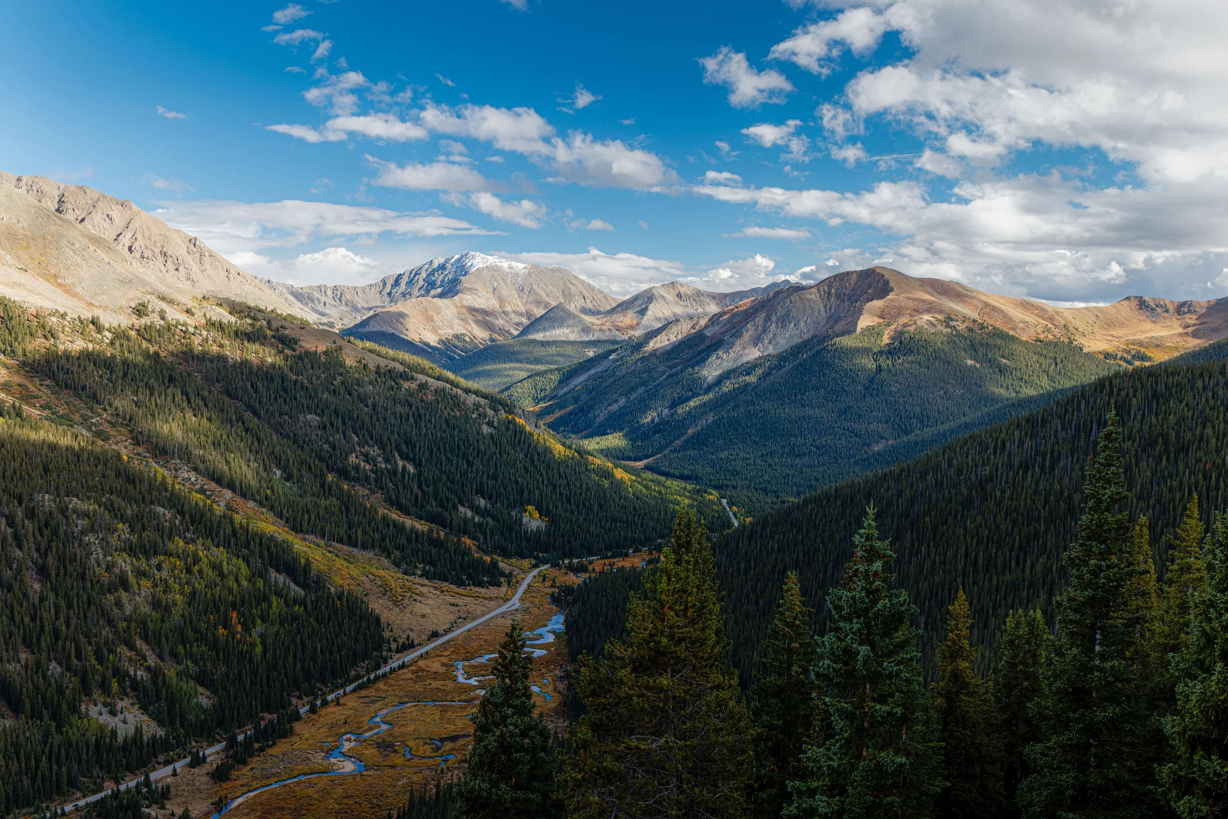 Scenic view of a valley surrounded by tall, forested mountains and a partly cloudy sky.