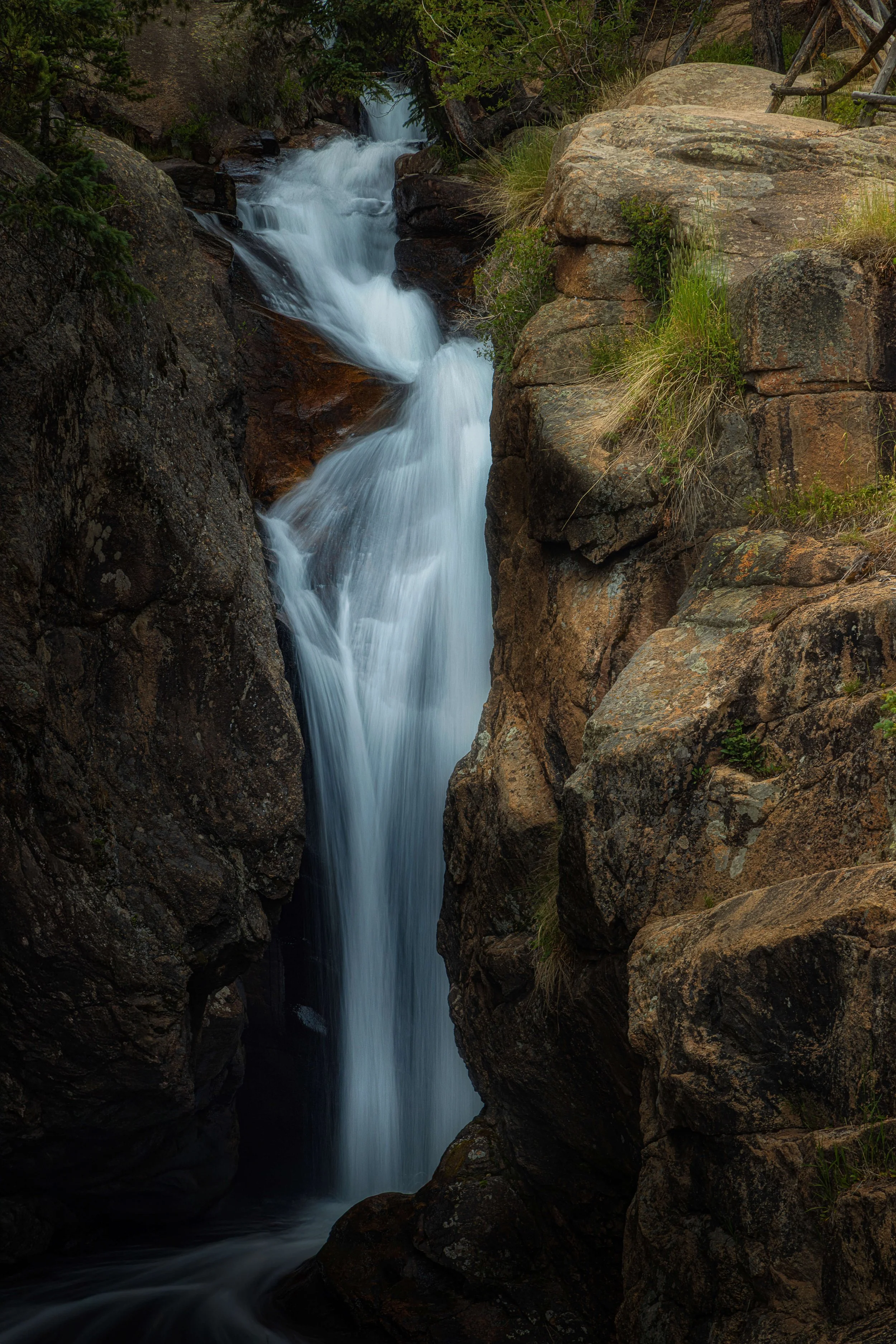 A narrow waterfall cascading between large rocks in a lush, green forest.