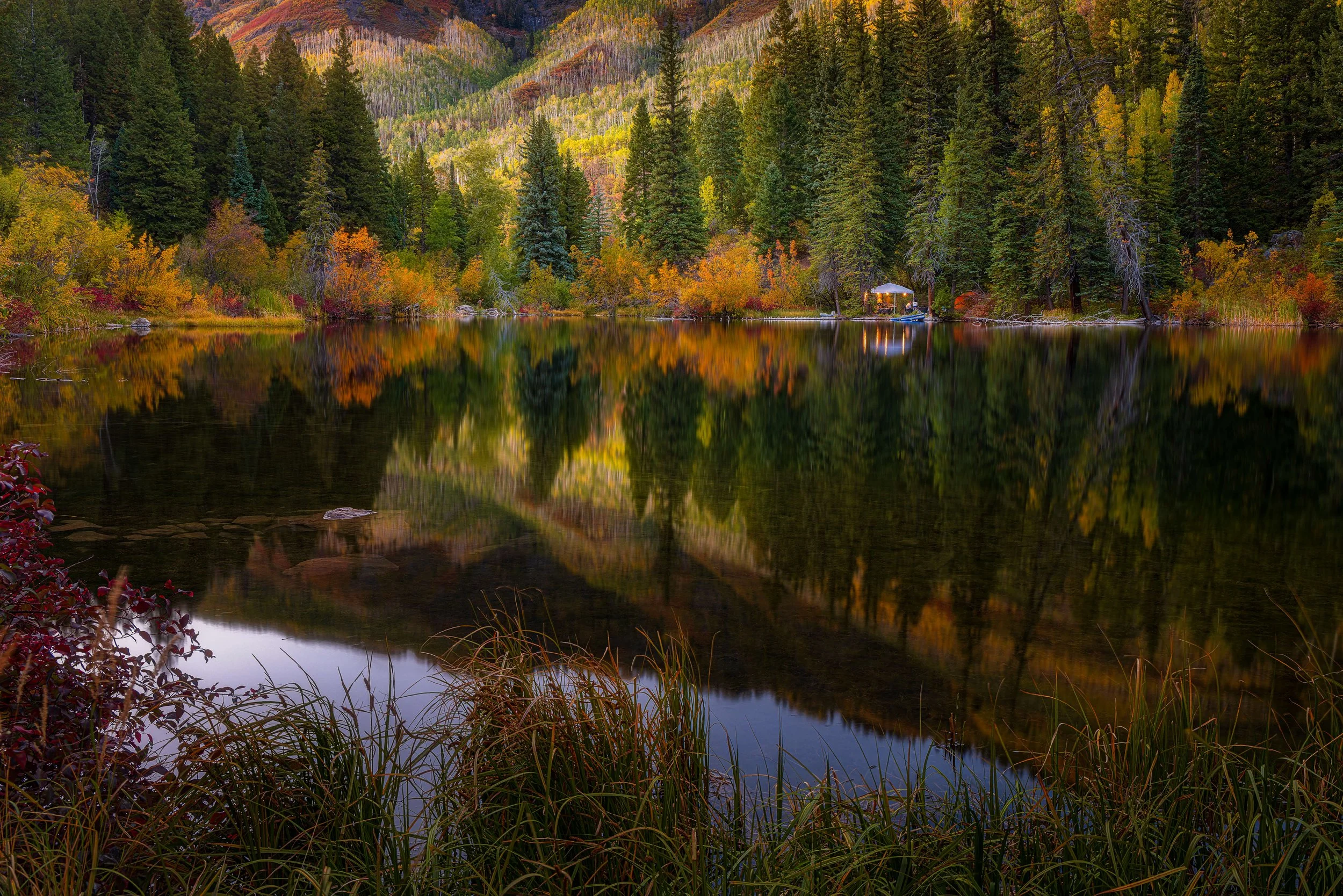 A serene mountain lake surrounded by autumn-colored trees, reflecting the vibrant foliage and mountains on a calm water surface.