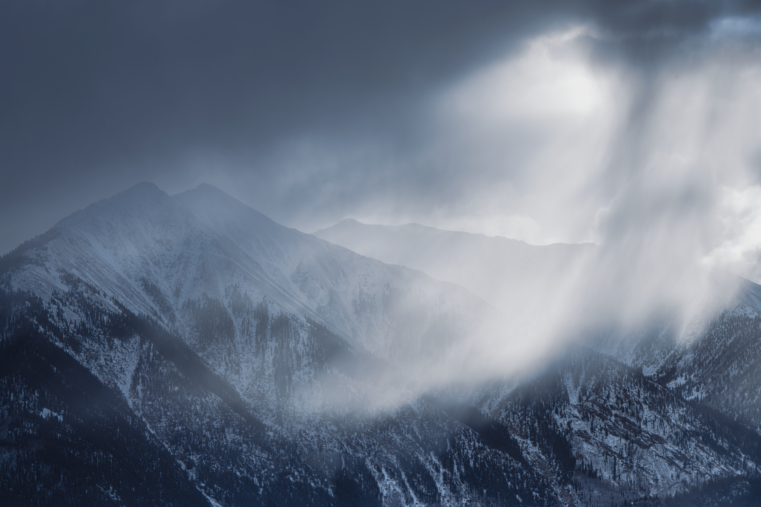 Snow-covered mountain peaks with dark clouds and mist.