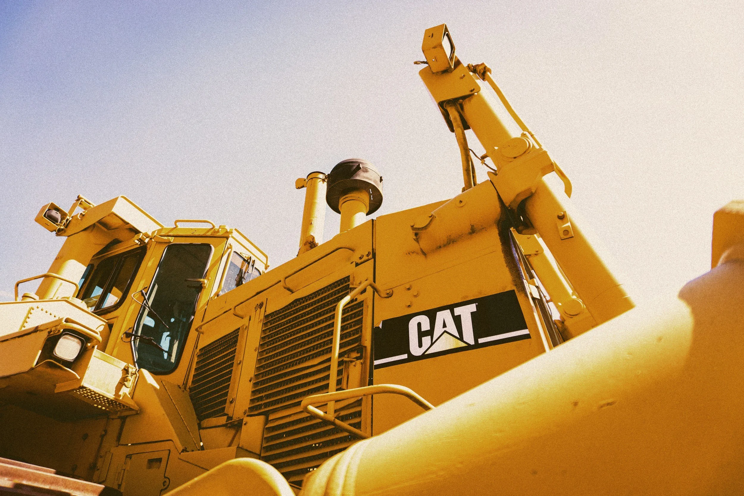 Close-up of a yellow Caterpillar (CAT) bulldozer from a low angle, showing the cabin and engine parts.