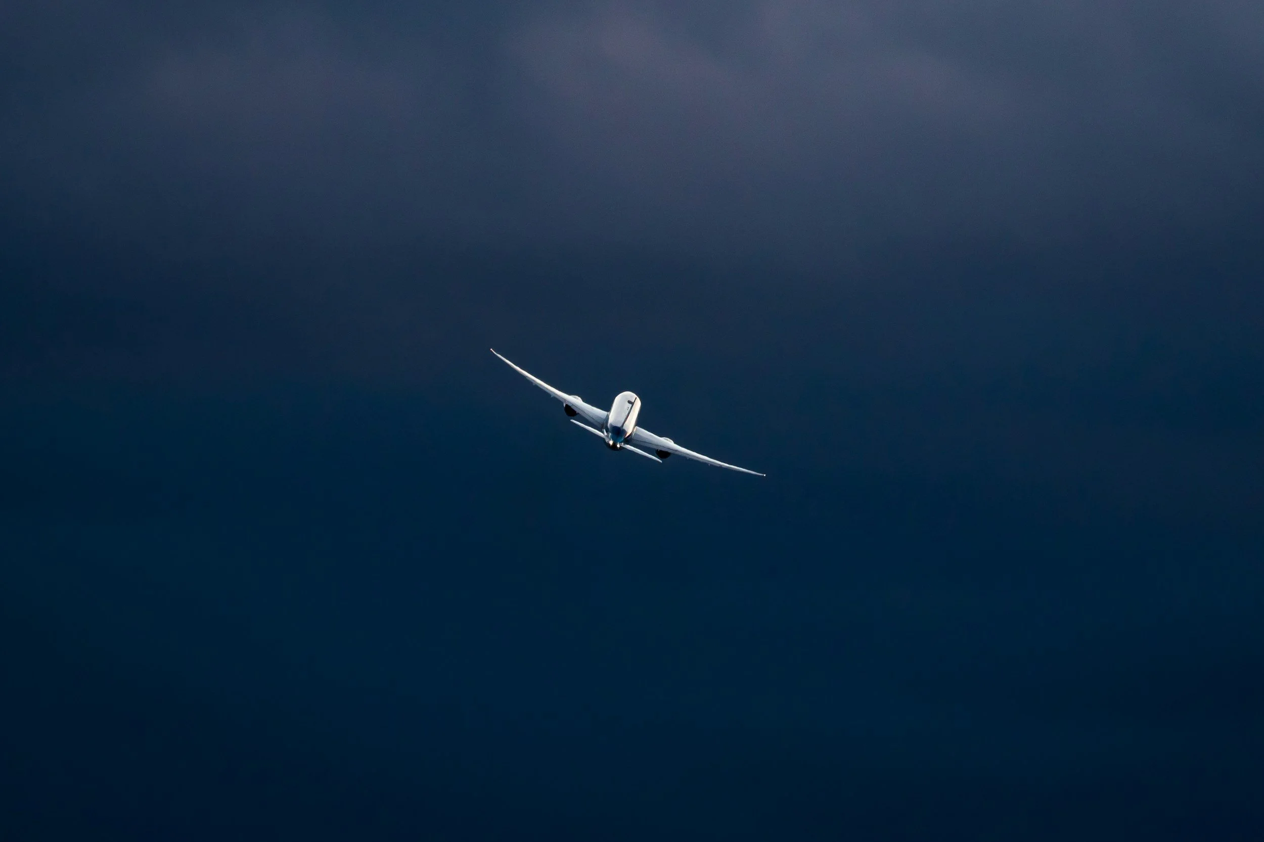 A white airplane flying through dark, cloudy skies.