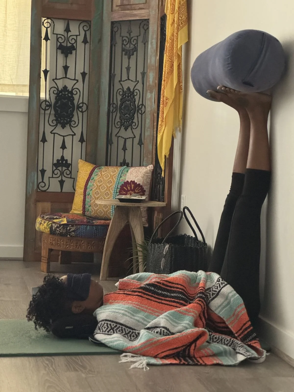 A woman practicing yoga on a mat in a studio, being filmed by a person holding a camera.