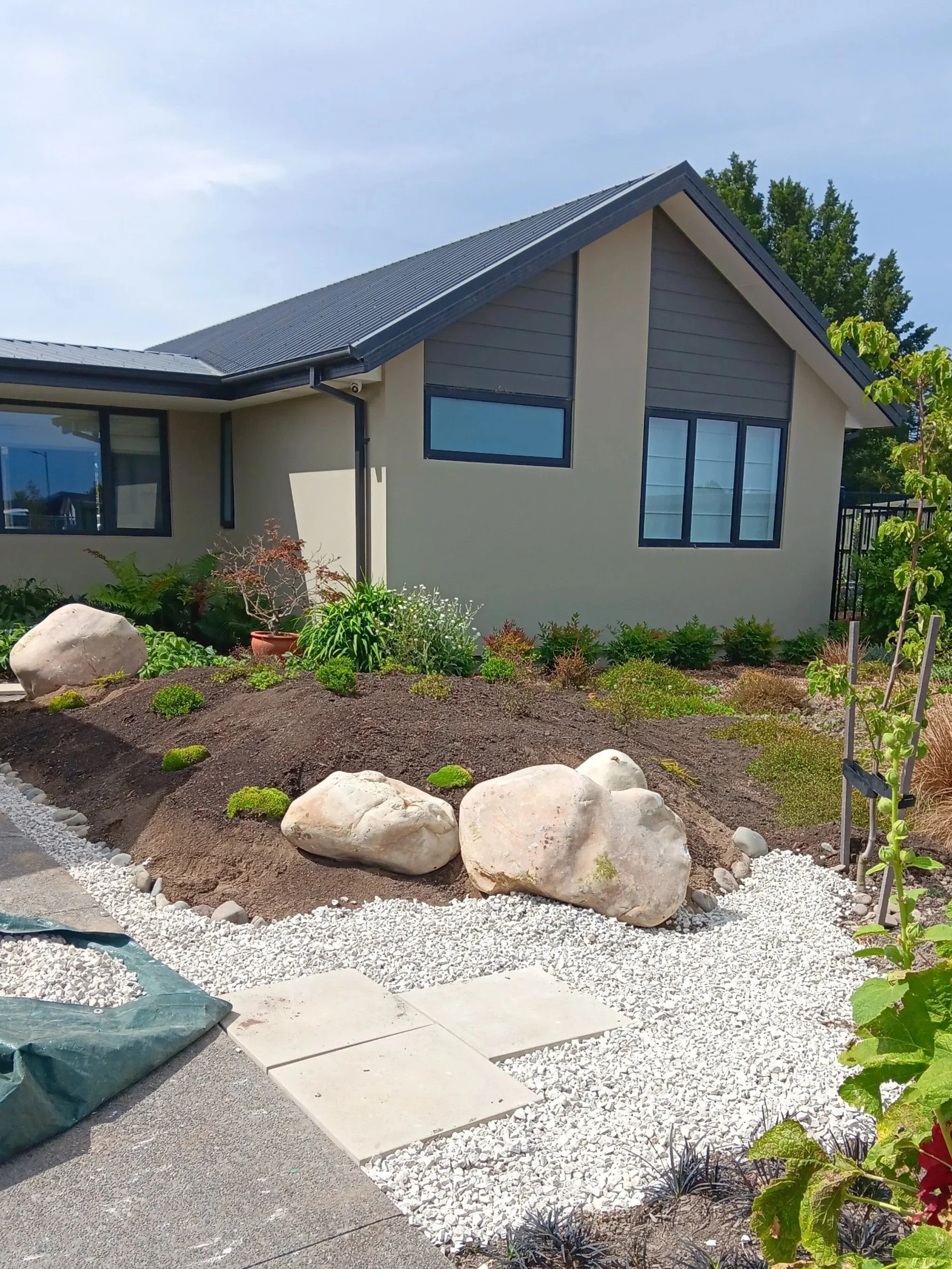 Landscape view of a modern house with a garden, large rocks, and a gravel path