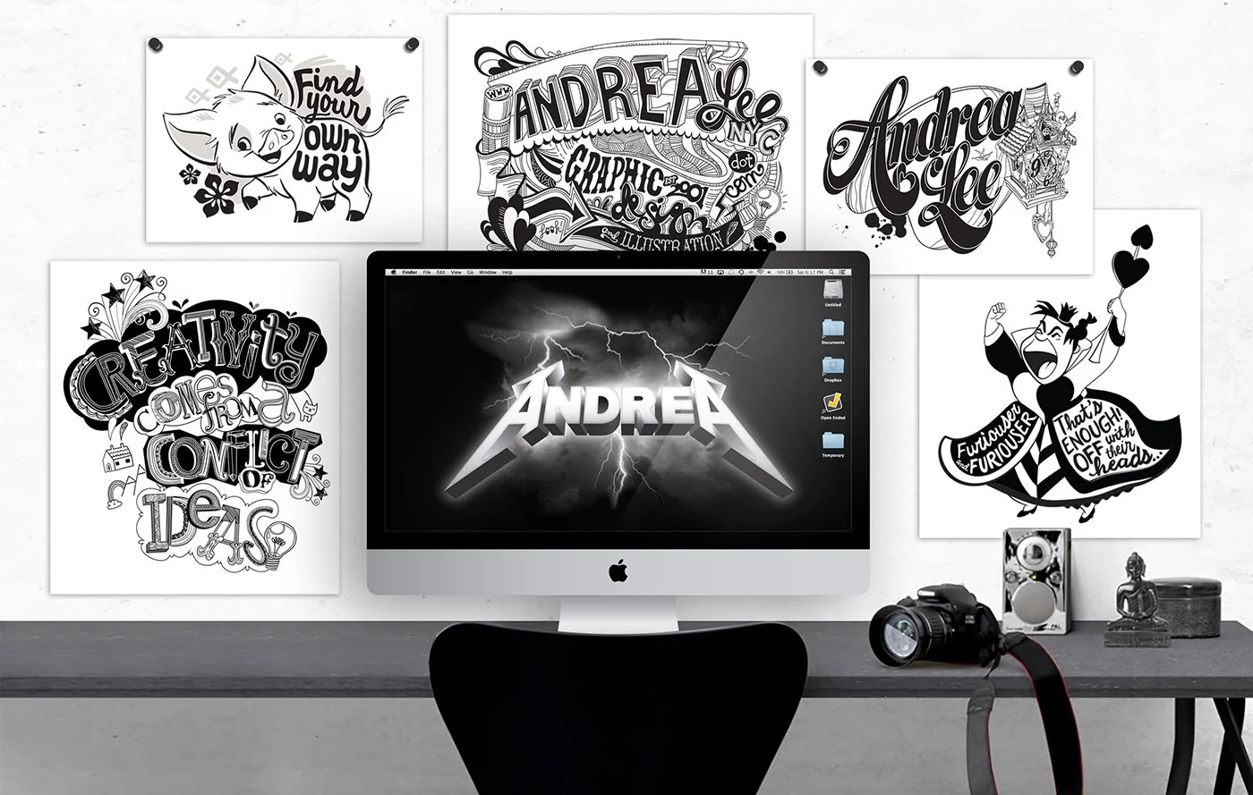 A workspace desk with a computer monitor displaying the name "Andrea" with lightning graphics. The wall behind the desk features five black-and-white posters with various artistic and typographic designs.