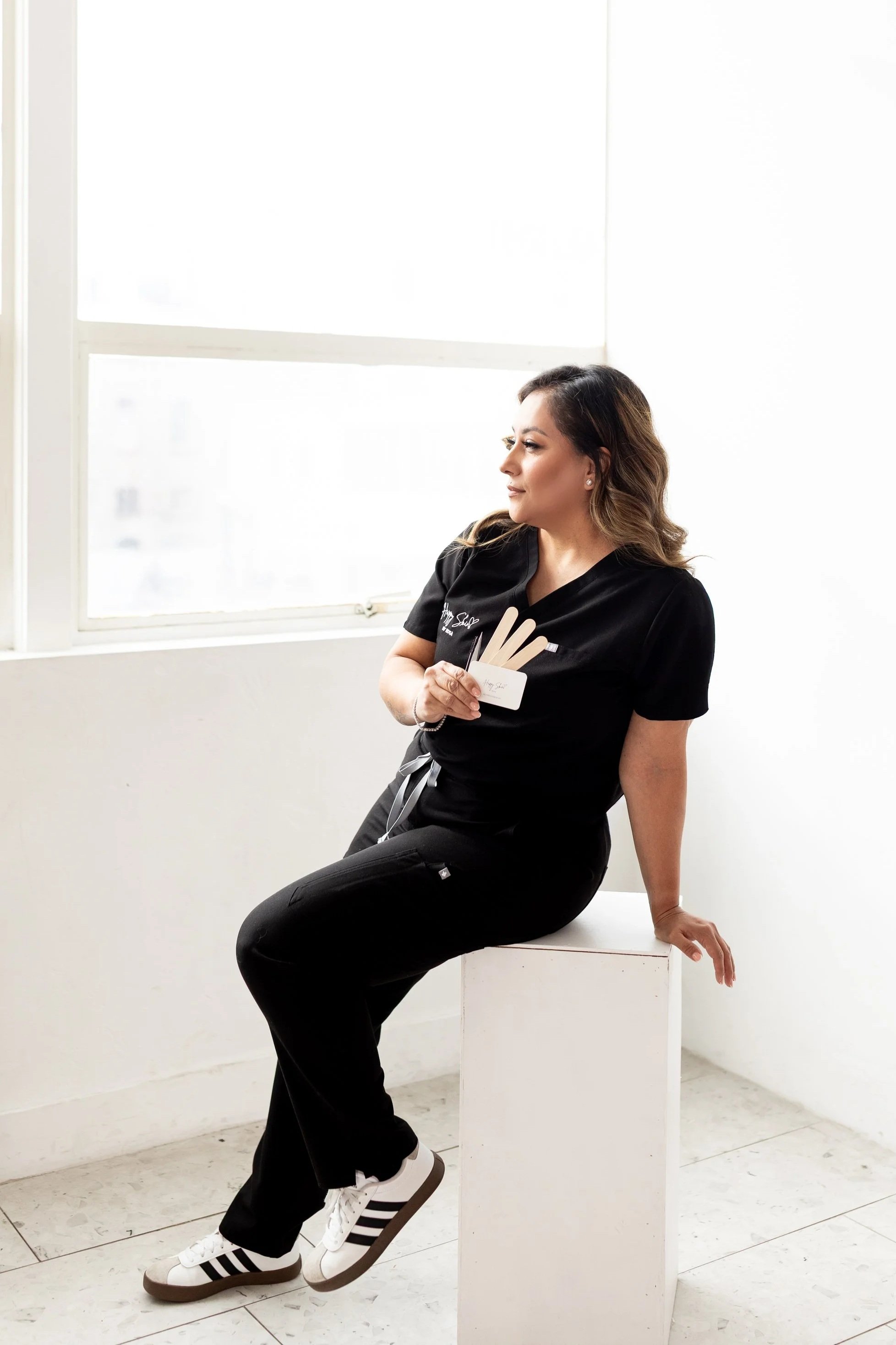 Esthetician in black scrubs holding waxing tools in studio