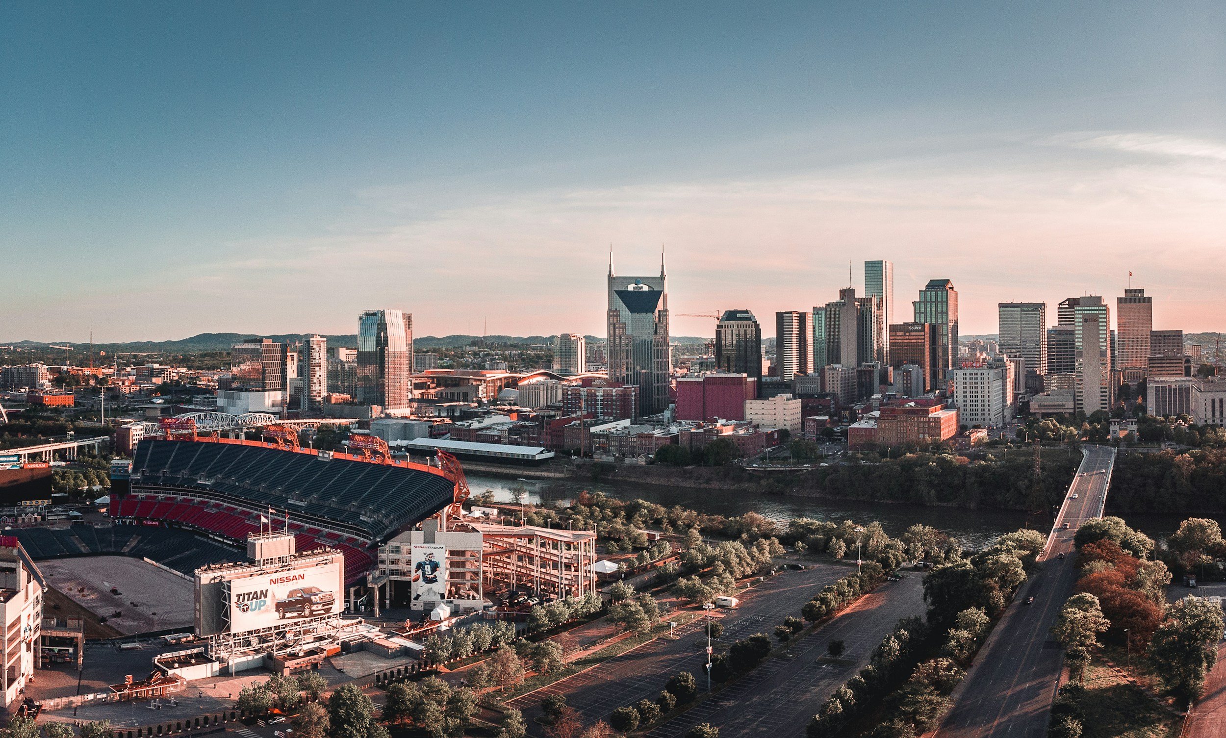 Skyline of Nashville, Tennessee with downtown skyscrapers and Nissan Stadium in the foreground at sunset.