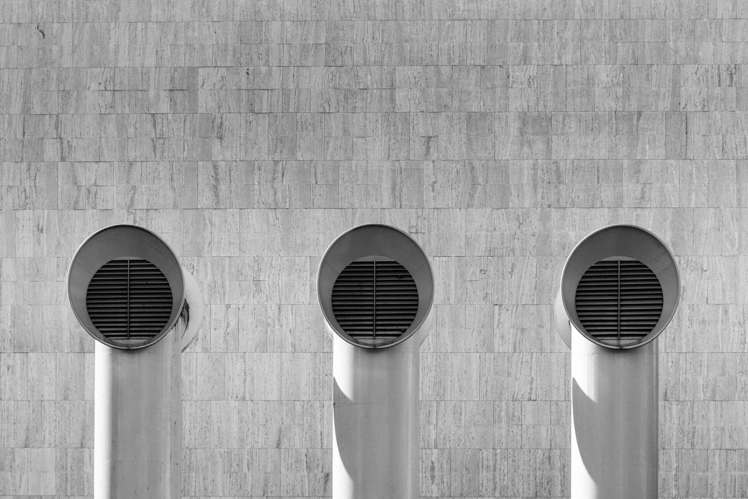 Three large circular vents on a textured concrete wall.