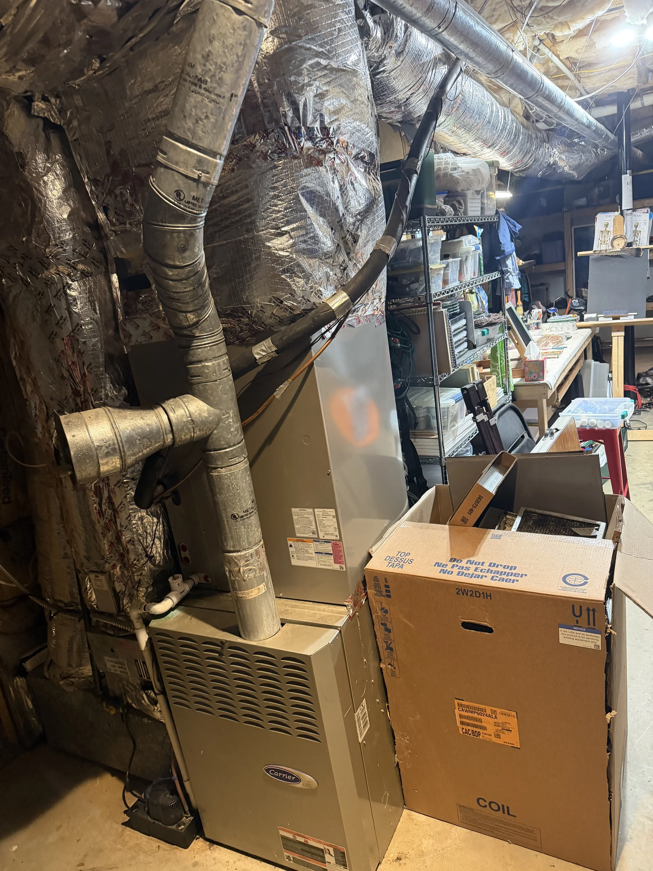 A utility room with a furnace, ductwork, and storage shelves filled with various items, including boxes, tools, and household supplies.