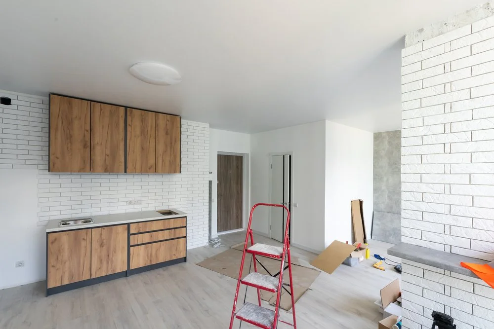 Interior of a room under renovation with white brick walls, wooden cabinets, a red step ladder, and various construction tools and materials.