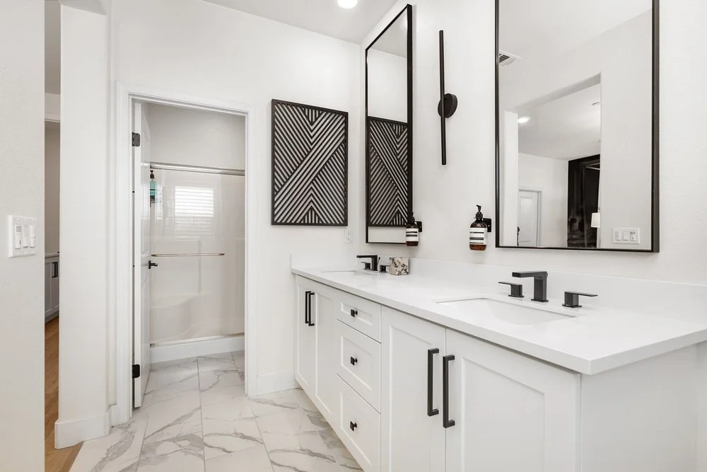 Modern bathroom with white cabinetry, black hardware, two large mirrors, and black wall art.