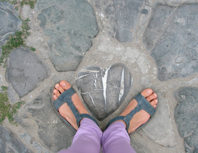 This is an image of a woman standing on the ground surrounding a heart stone.