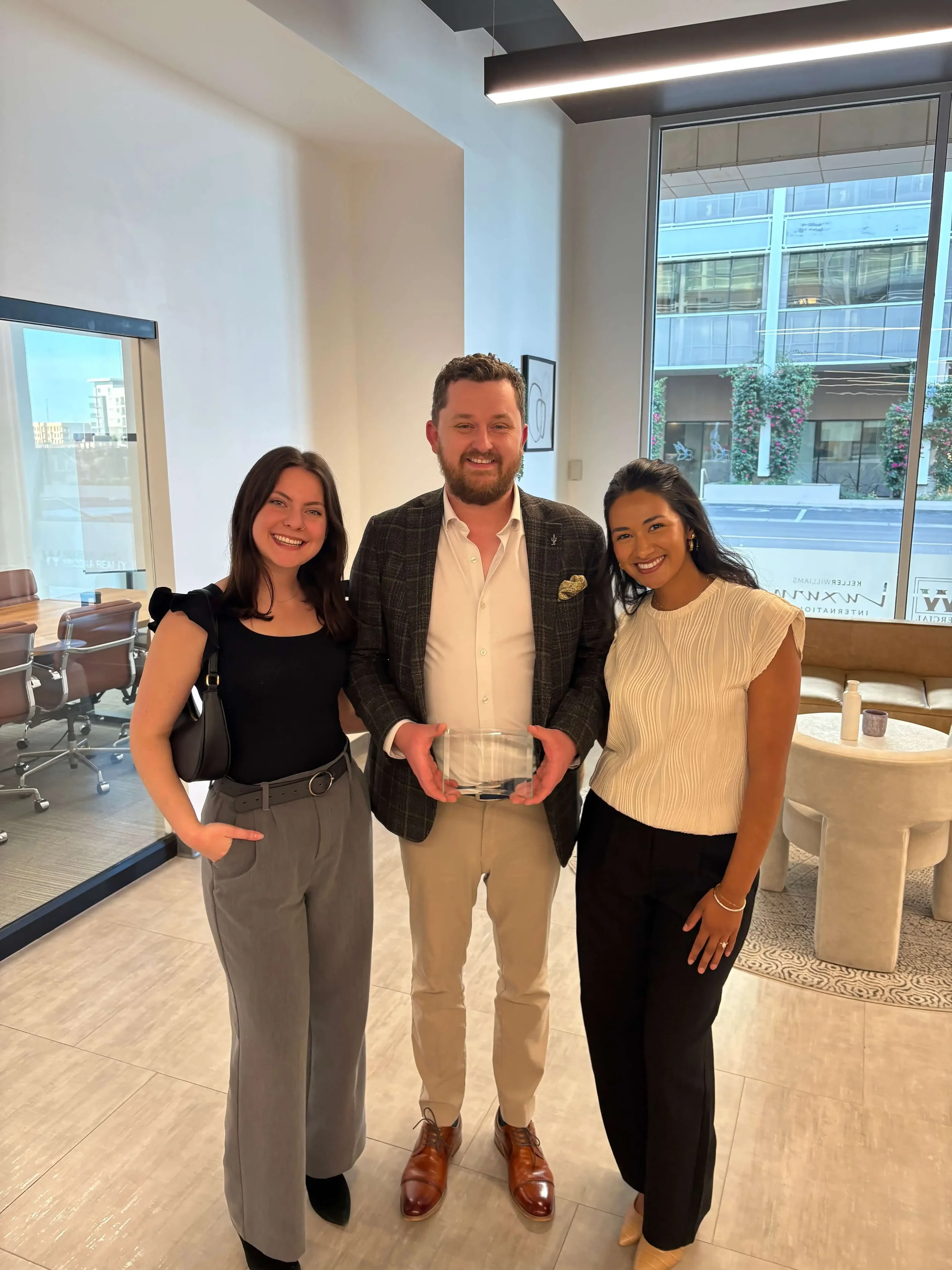 The Bryant Real Estate team smiling together while holding a glass top-performer award in a modern Phoenix office setting.