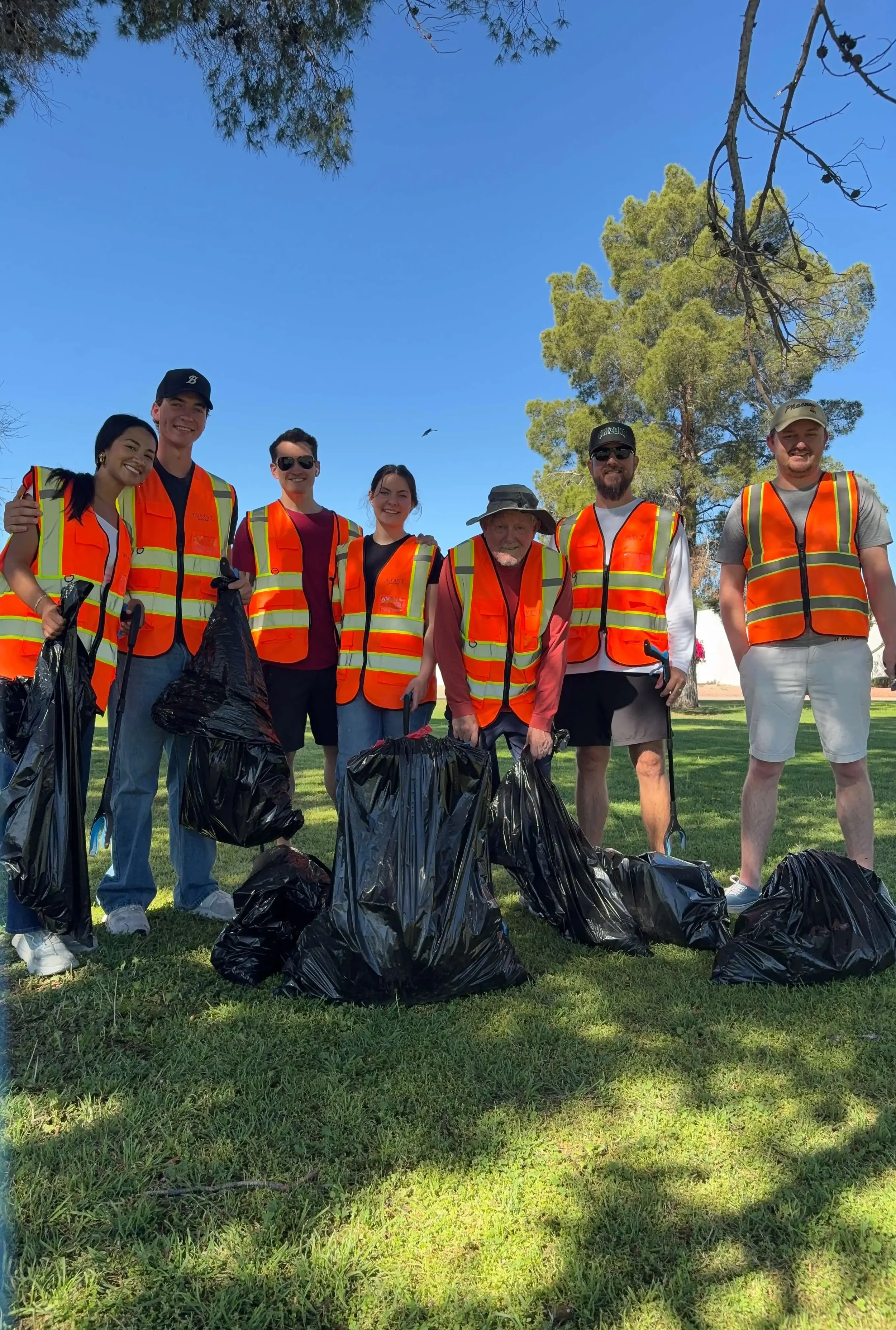 The Bryant Real Estate team standing together in orange safety vests with trash bags during a neighborhood community cleanup event in Phoenix.