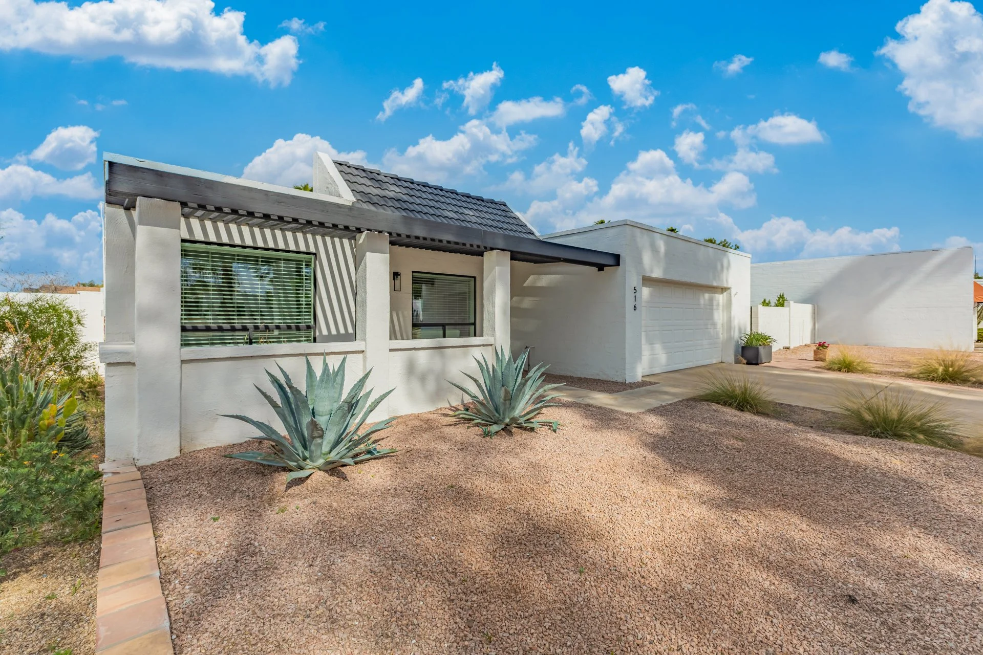 Front exterior of a renovated modern ranch-style home featuring a two-car garage, architectural pergola, and low-maintenance desert landscaping.