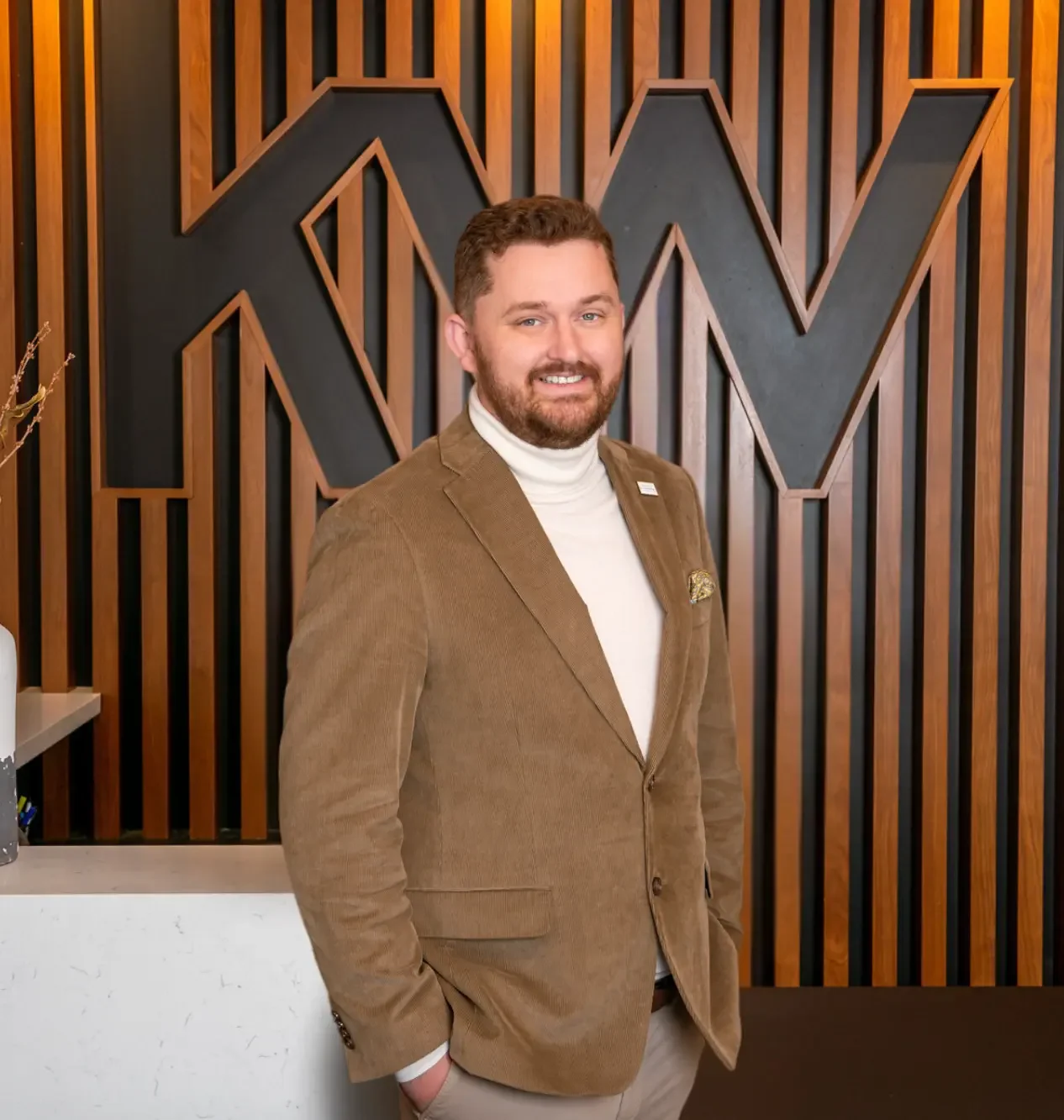 Scott Bryant wearing a tan suit in front of a KW sign.