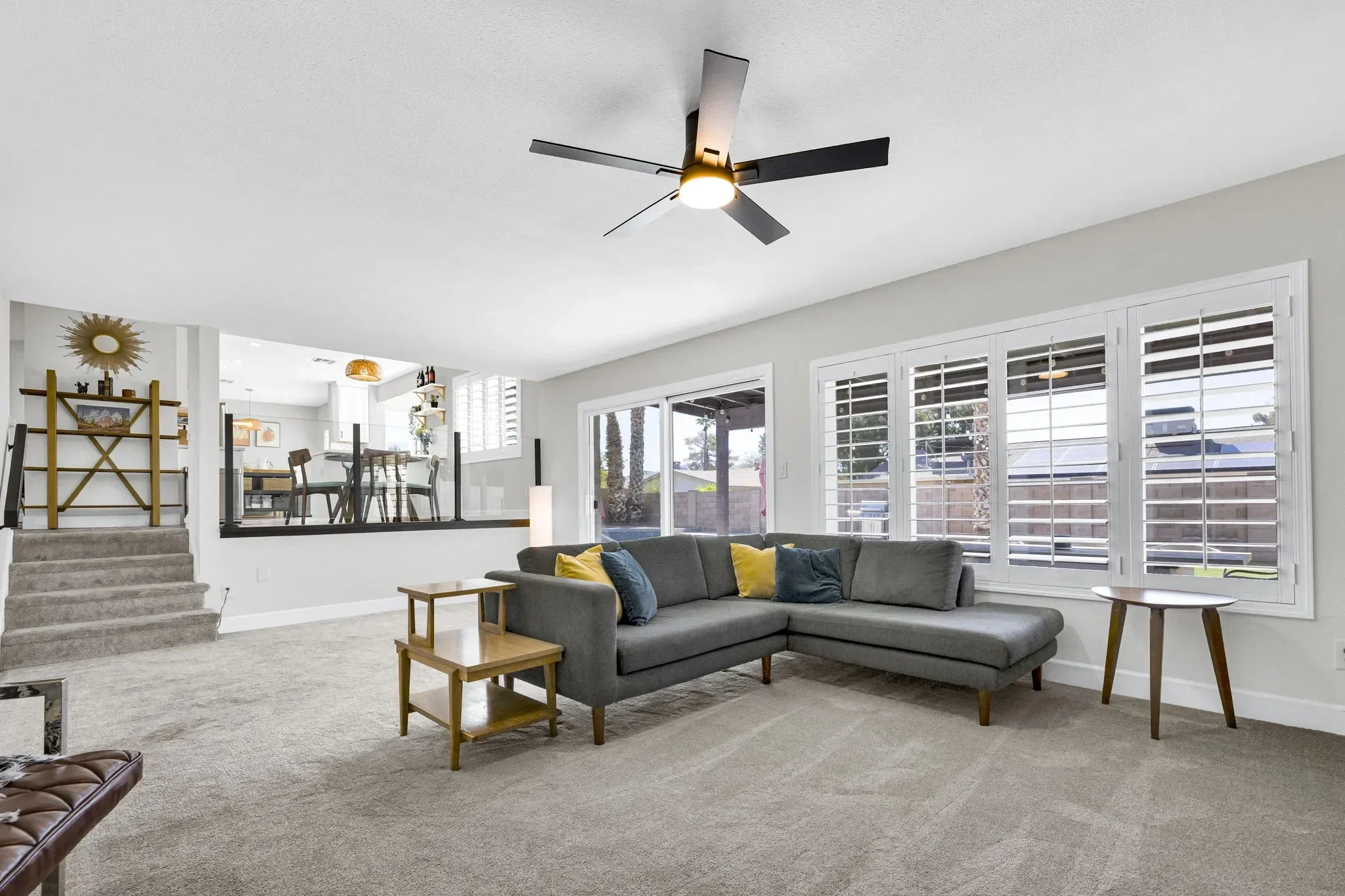 Bright, open-concept living room featuring a grey L-shaped sofa and stairs leading to an elevated kitchen.