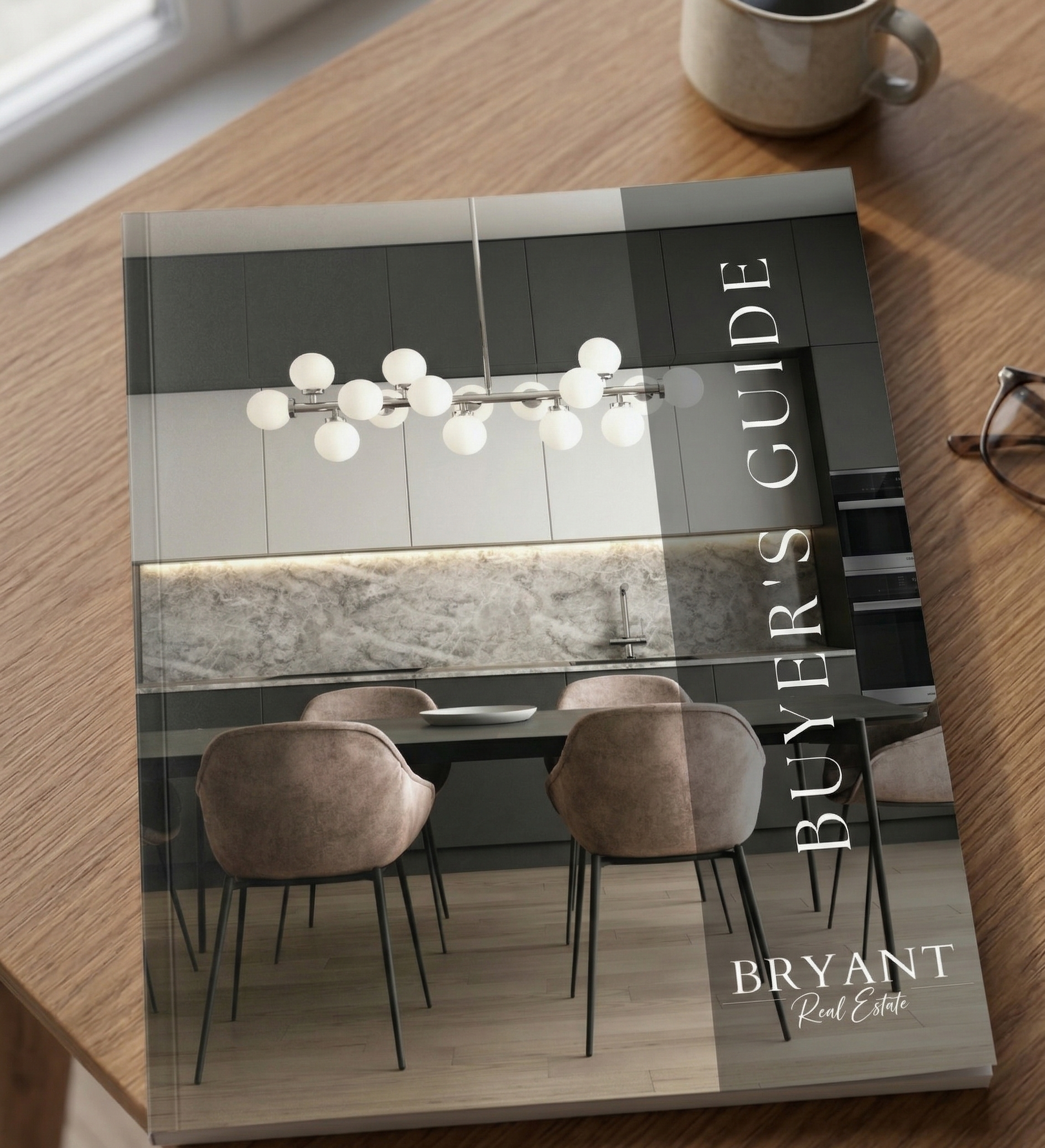 A printed, hardcover Real Estate "Buyer's Guide" book by Bryant Real Estate is angled slightly left on a wooden table, under warm sunlight, with a mug and glasses nearby.