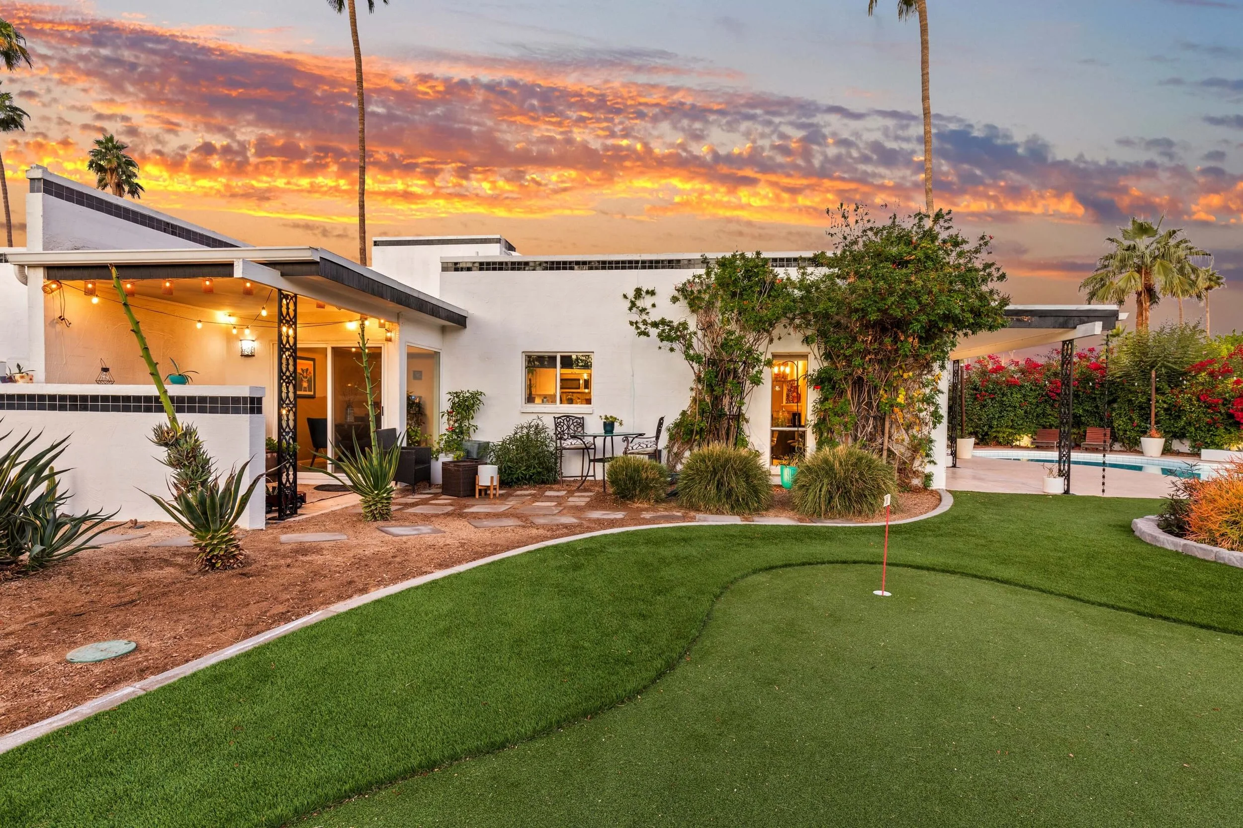 The twilight exterior of a modern luxury home in Phoenix, Arizona, featuring a beautifully landscaped backyard putting green and vibrant sunset sky.