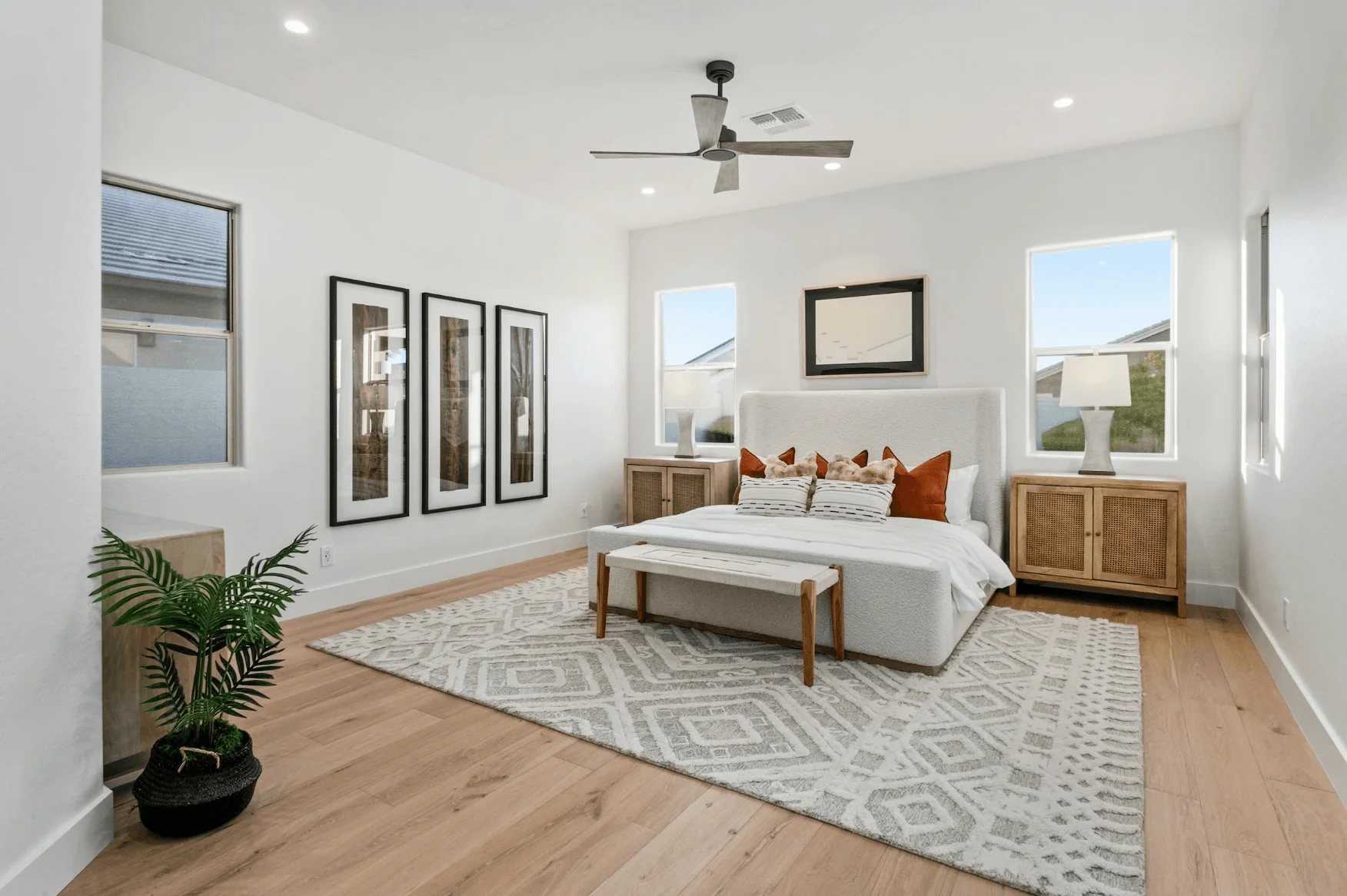 Bright and modern main bedroom with neutral decor, wooden nightstands, elegant framed wall art, and large windows bringing in natural light.