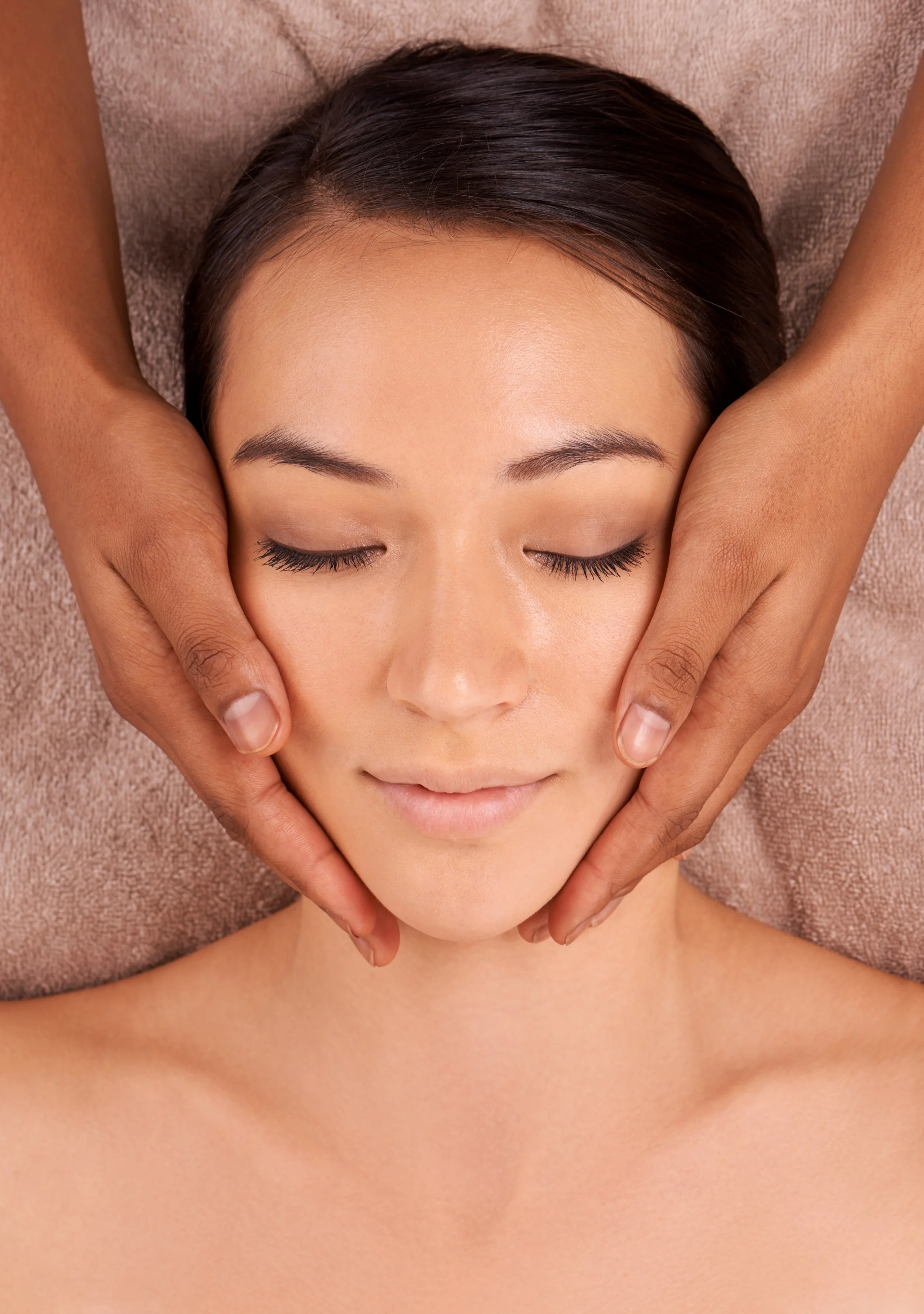 A woman receiving a massage with her eyes closed, lying on a massage table with a soft towel under her head.
