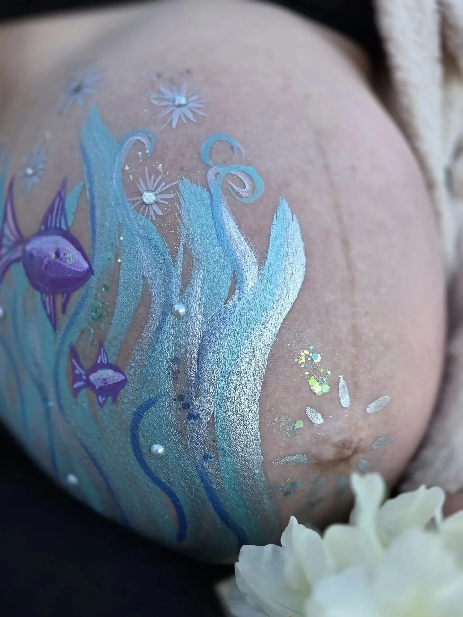 a pregnant woman's painted belly, adorned with fish, seaweed and sparkles