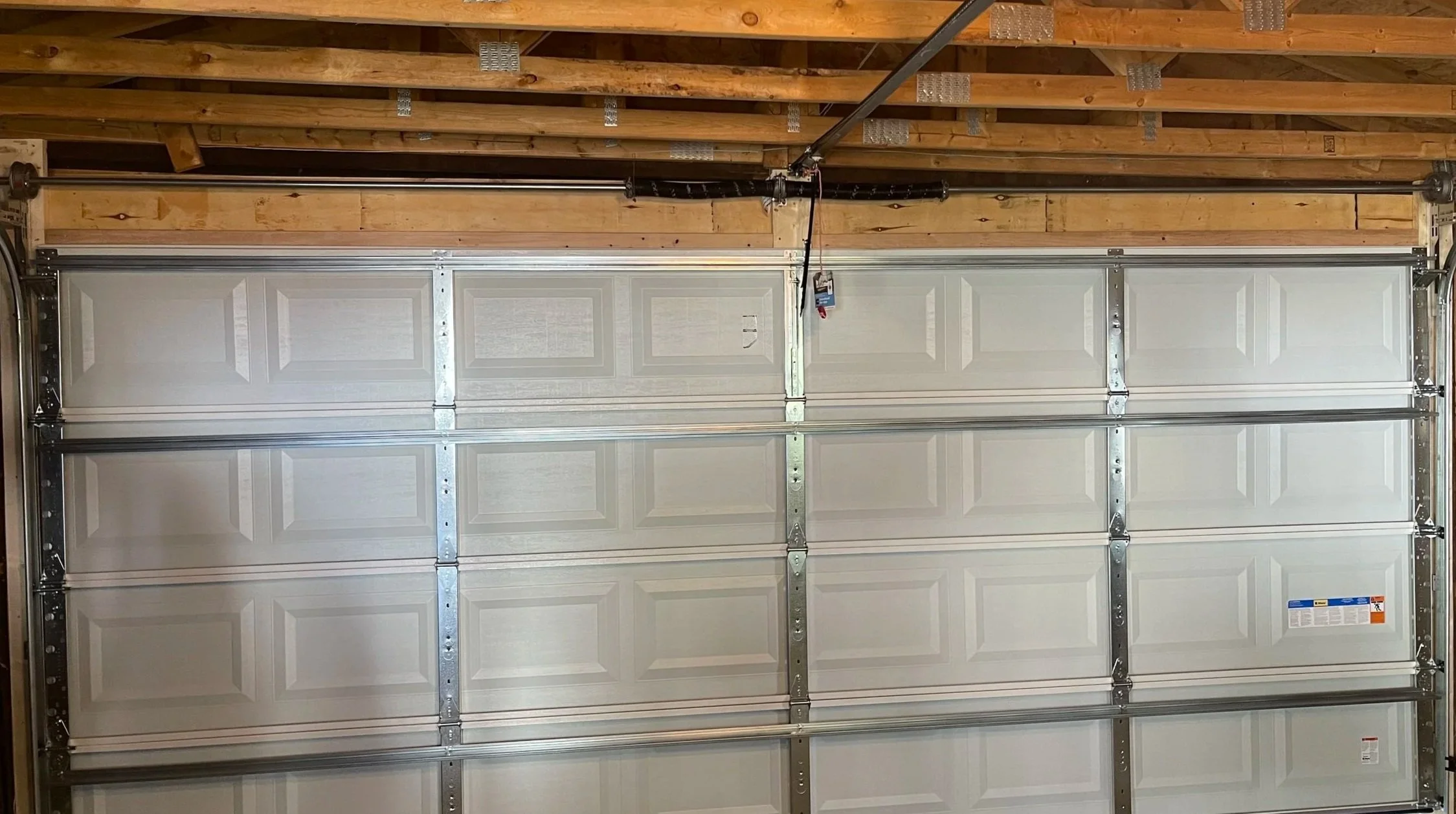 Interior of a garage focused on the spring assembly above a white 18 by 7 door