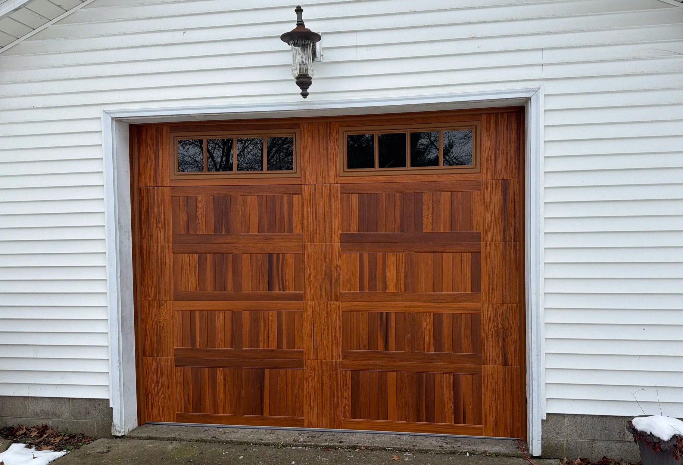Wood-grain 8 by 7 garage door with windows in the top section surrounded by a white building