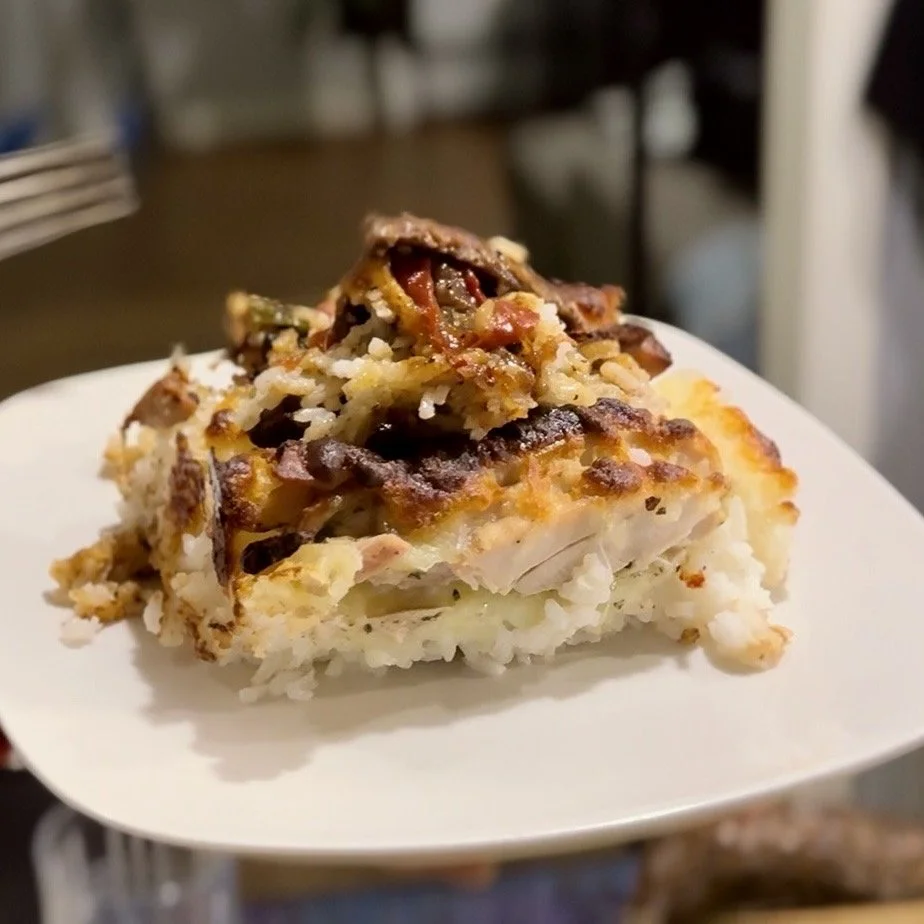 A slice of homemade casserole with layers of rice, vegetables, melted cheese, and topped with cooked ground meat and tomato slices on a white plate
