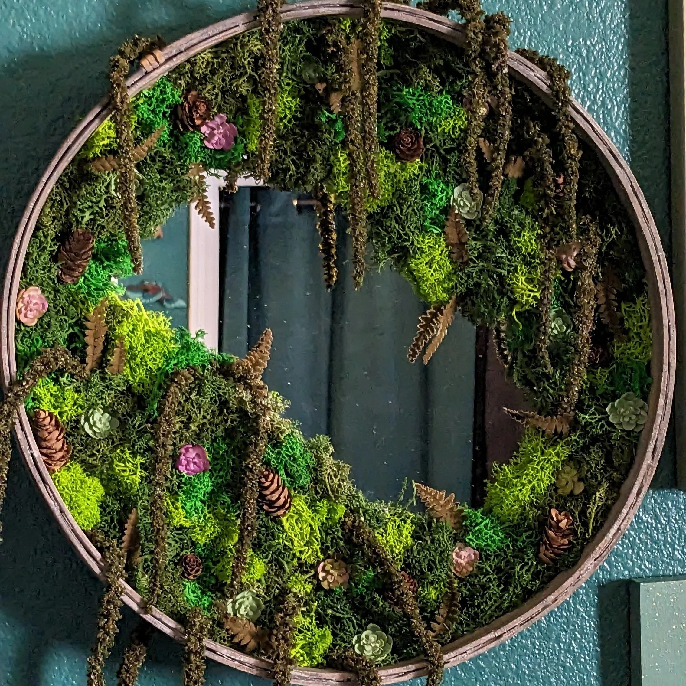Decorative circular wall hanging with preserved moss, succulents, pinecones, and dried flowers inside a wooden frame.