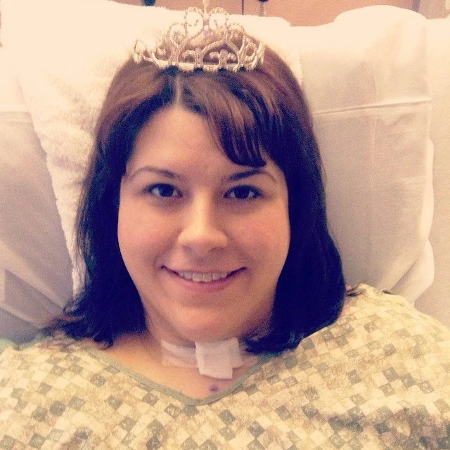 Woman lying in hospital bed wearing a crown and smiling.