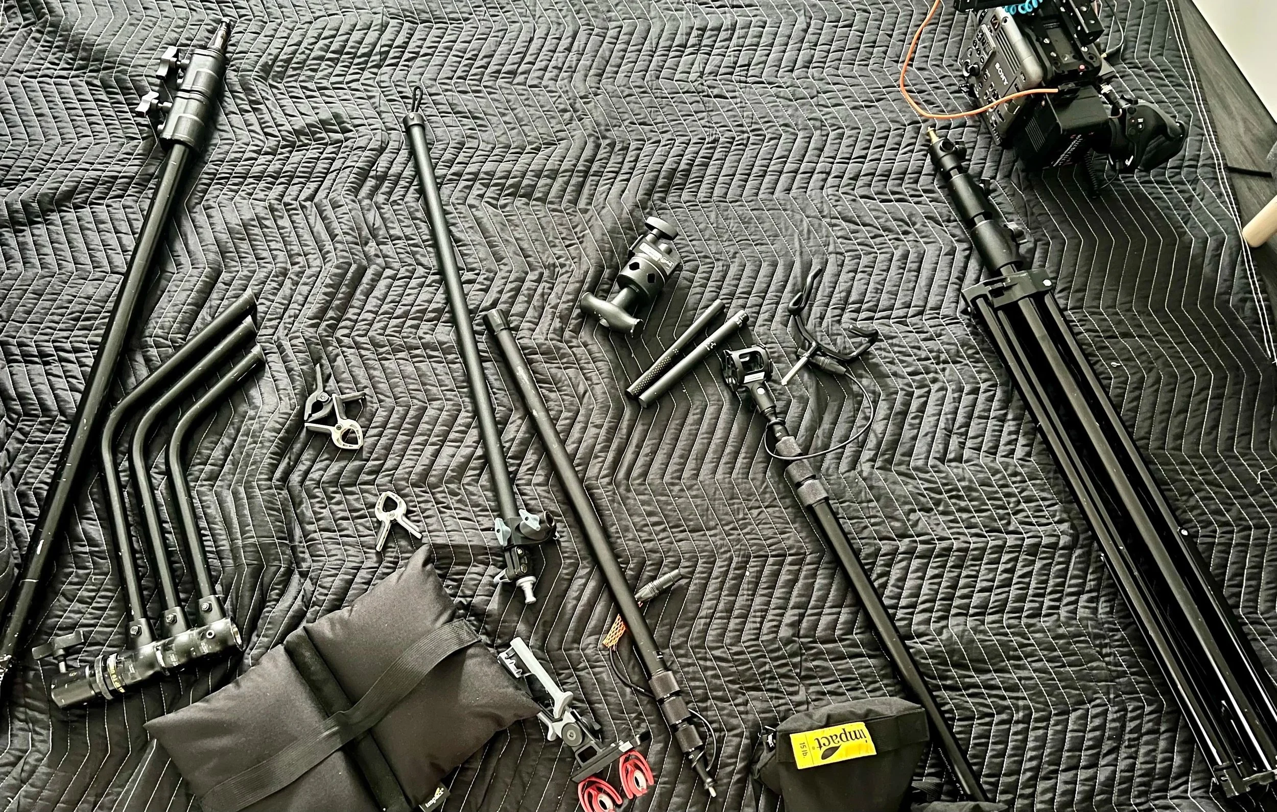Camera and filming equipment, including tripods, a camera, and accessories, spread out on a quilted surface.