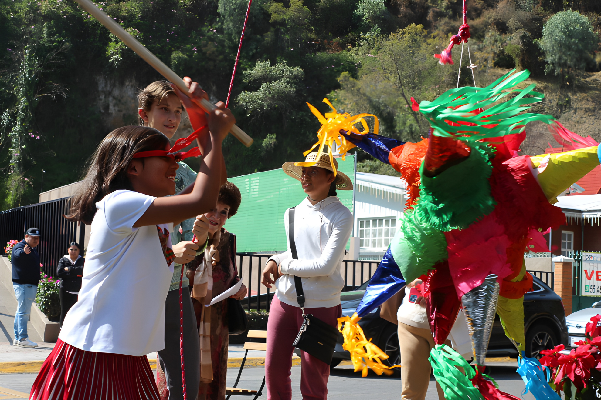 Children and adults celebrating outdoors with a colorful piñata on a sunny day.
