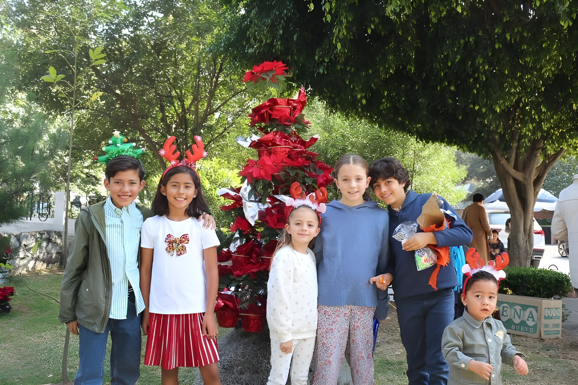 Group of six children celebrating Christmas outdoors with a decorated Christmas tree and holiday accessories.