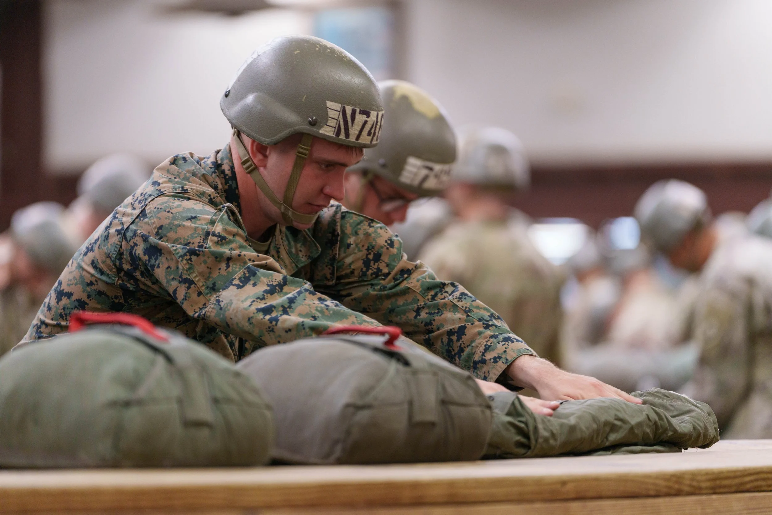 Soldiers in military uniforms and helmets practicing first aid on stretchers in a training facility.