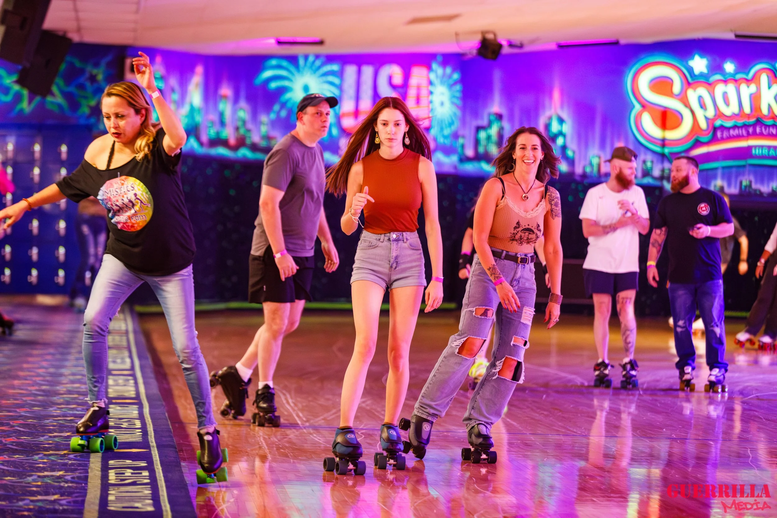People roller skating inside an amusement park with colorful lights and signs, including a sign that reads 'Spark.' They are enjoying a fun, lively atmosphere.