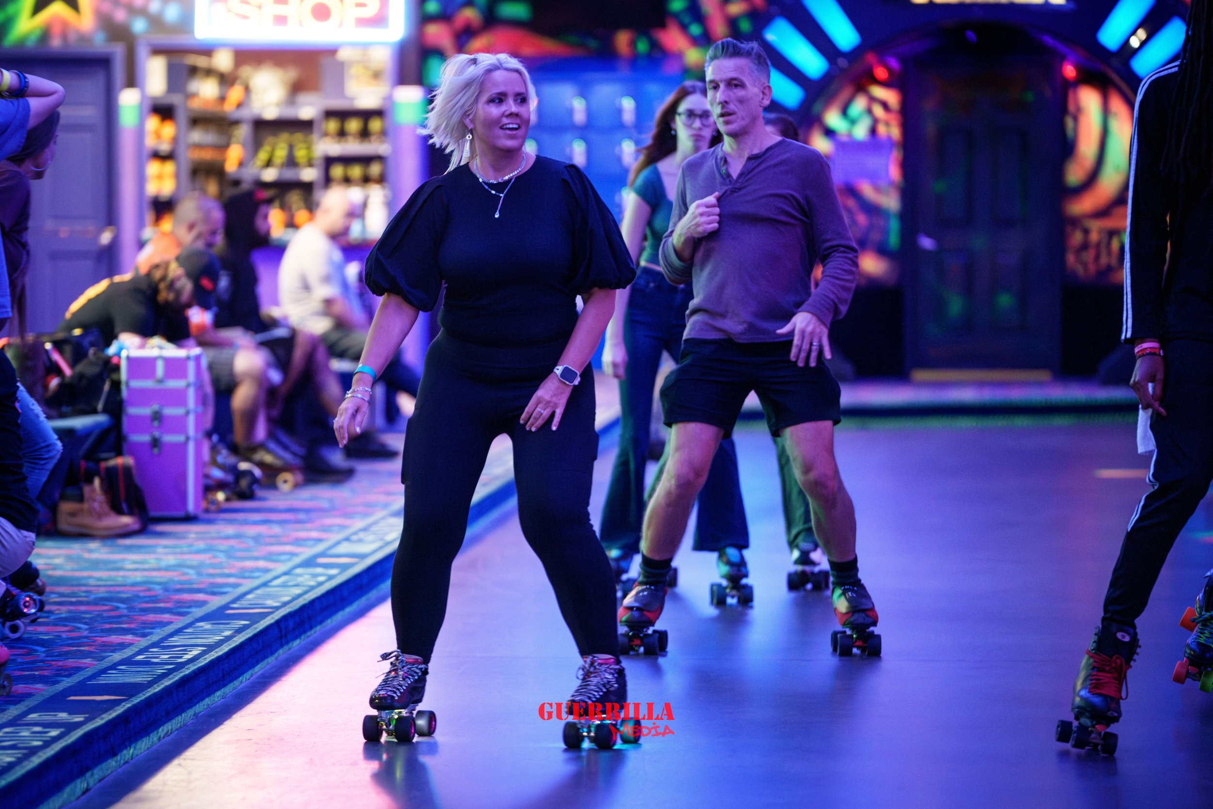 People roller skating in an indoor skate rink with colorful neon lights and a vibrant atmosphere.