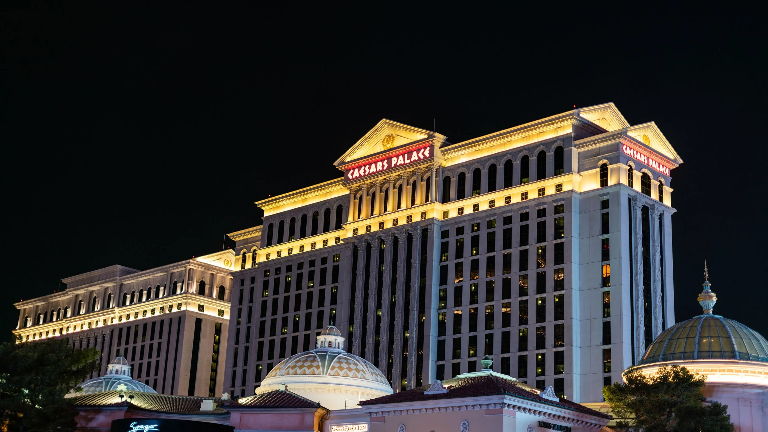 Night view of the illuminated Caesars Palace hotel and casino in Las Vegas, featuring its classical architectural style with domes and columns.