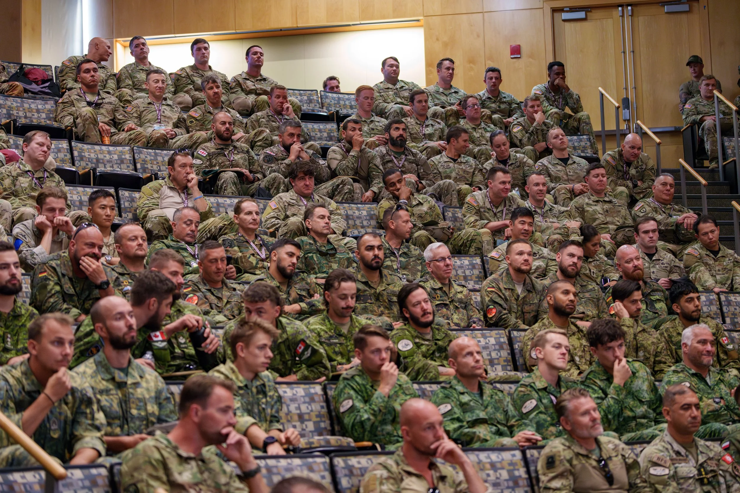 A group of military personnel sitting in an auditorium, attentively listening to a presentation or speech.